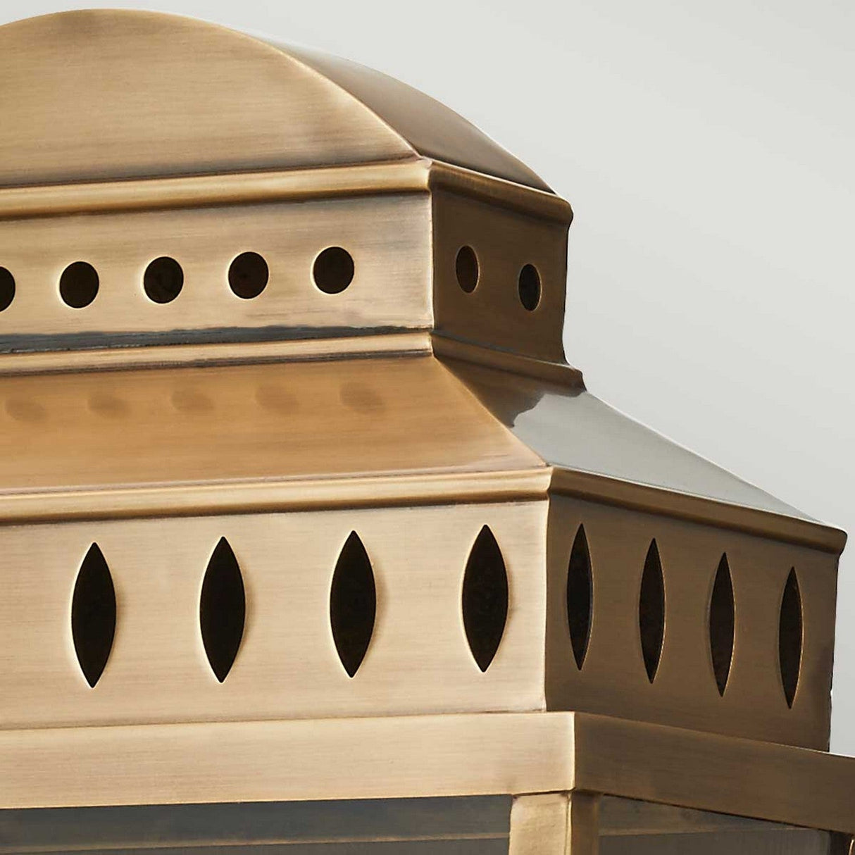 Close-up of the Mansion 2 Light Outdoor Wall Light in aged brass, showcasing a dome-shaped top adorned with circular and oval cutouts that provide both ventilation and decorative appeal. The polished yet slightly aged finish enhances its antique look, similar to an old-world brass lantern.