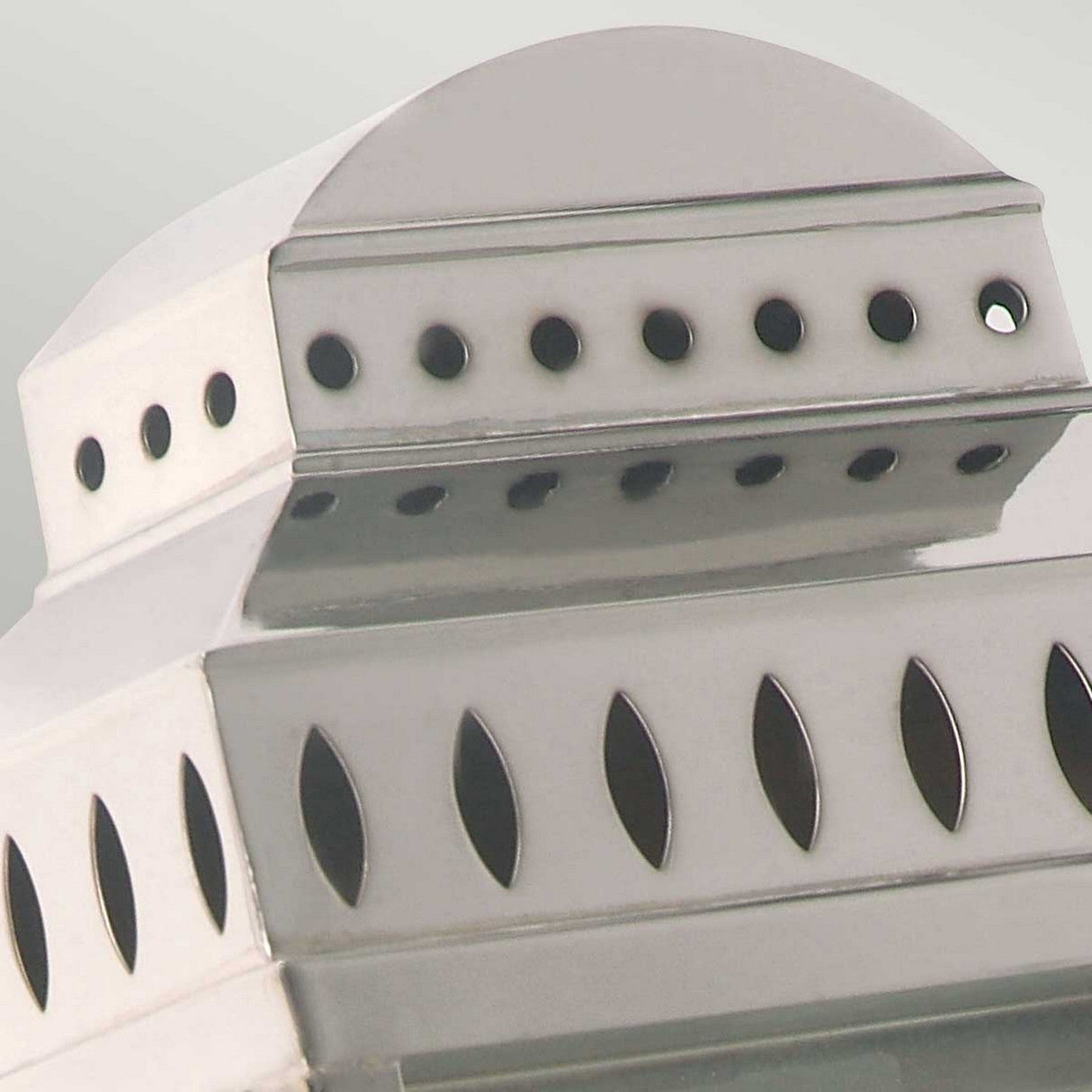 A close-up view of the Mansion 1 Light Outdoor Wall Light in polished nickel reveals its metallic structure adorned with geometric cut-out patterns, including circles and ovals, that cast shadows against a light background. The intricate design resembles an architectural feature.