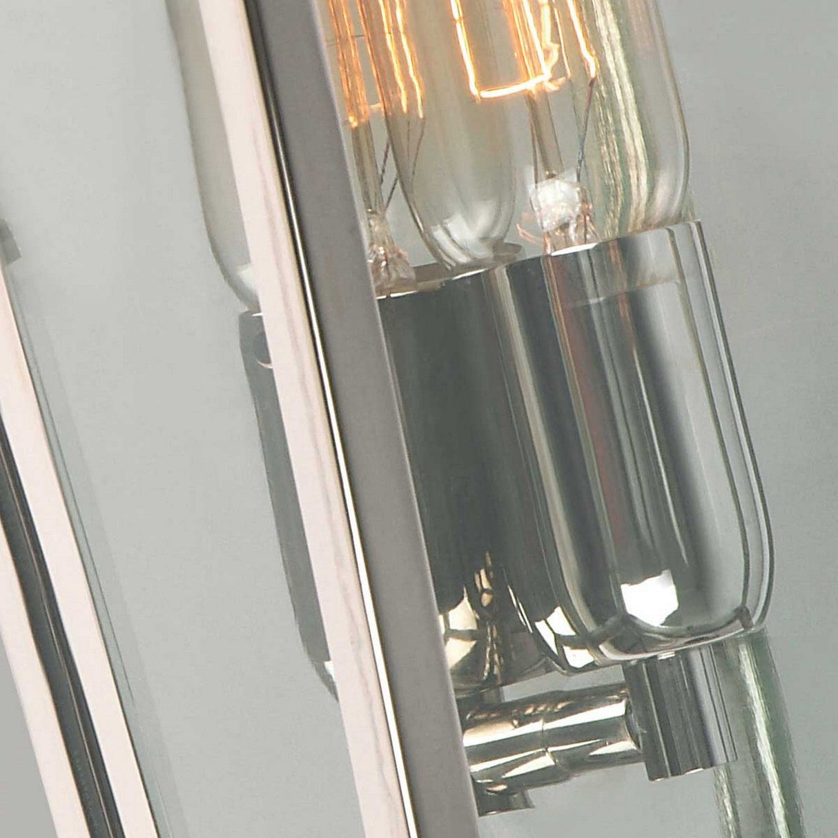 A close-up shows two vintage-style exposed light bulbs with glowing filaments, encased in a reflective glass fixture. These bulbs are part of the Mansion 1 Light Outdoor Wall Light, which features a polished nickel mount and clear glass panels, adding an elegant touch to any outdoor space.