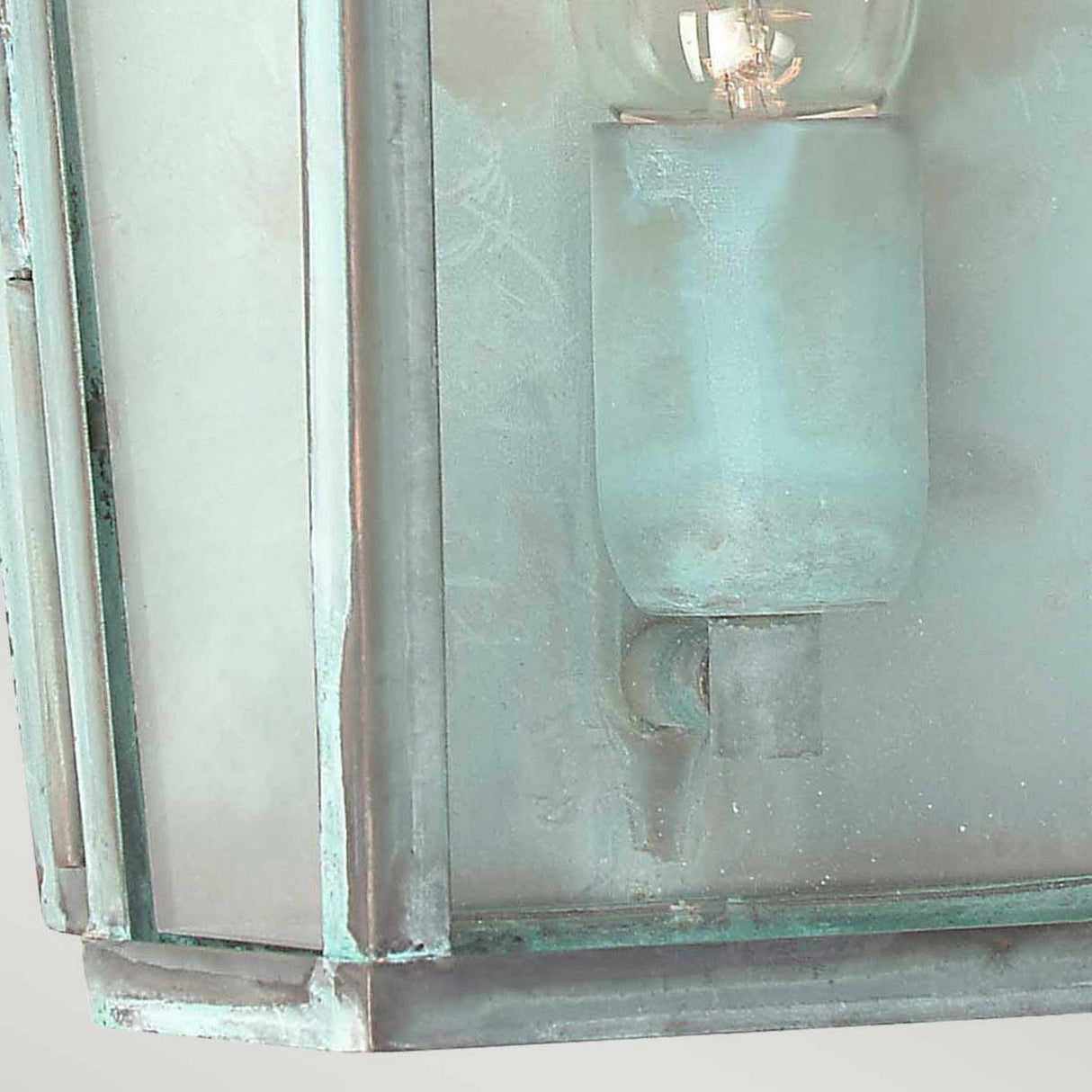 Close-up of the Mansion 1 Light Outdoor Wall Light in Verdigris finish, featuring a frosted glass and metal sconce with a visible light bulb. The design exudes vintage lantern aesthetics with its weathered appearance and solid brass frame, complete with a patina effect for an aged look.