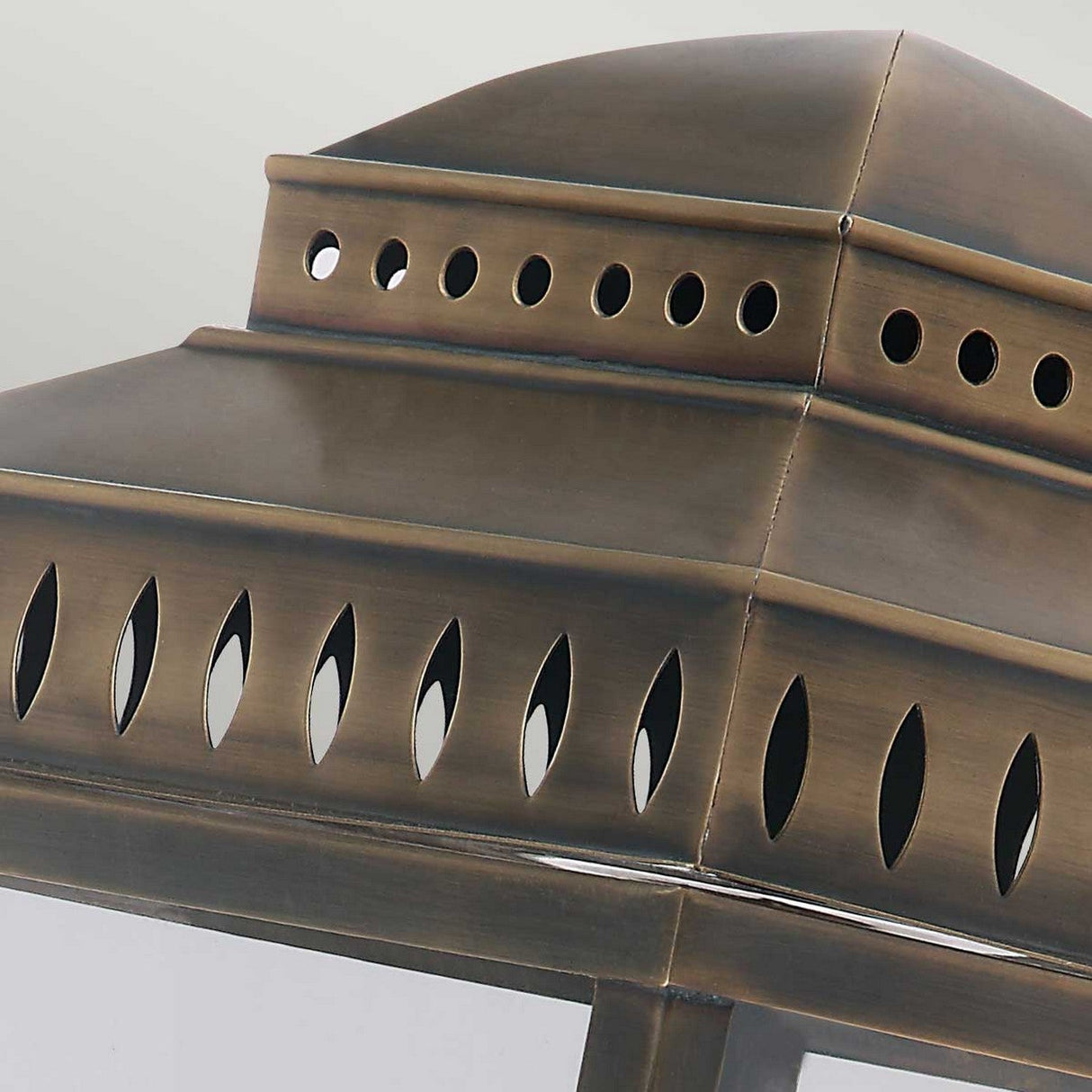 This detailed view showcases the Mansion 3 Light Outdoor Wall Light in an aged brass finish. The lantern boasts a tiered, square top with small circular holes and elongated oval patterns, capturing British design elements with a vintage, ornate touch. It's ideal for adding timeless charm to your outdoor spaces.