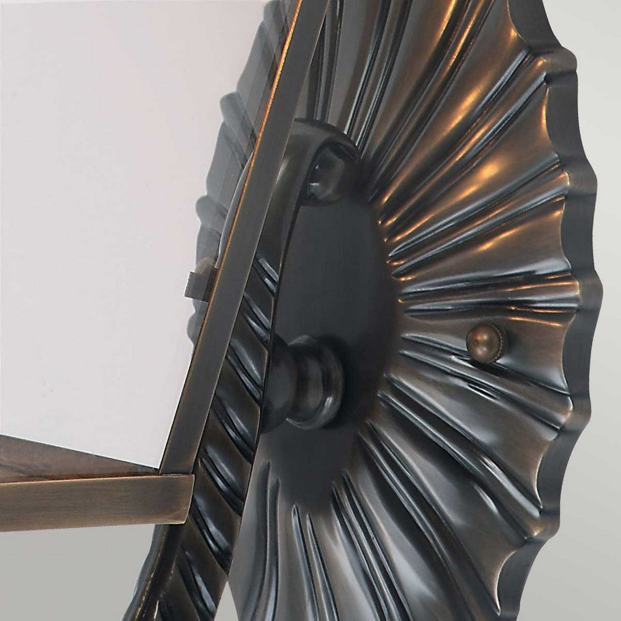The Mansion 3 Light Outdoor Wall Light in aged brass showcases a decorative design with a circular, radial appearance. The ridged metallic surface features a bronze finish and houses a flat piece of glass within its metal frame. Its candle-style lamp holders add an elegant touch against the soft neutral background.