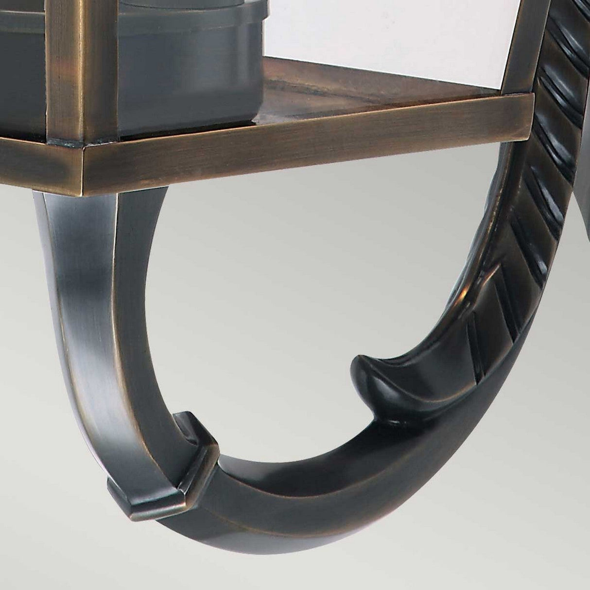 Close-up of the Mansion 3 Light Outdoor Wall Light in aged brass, showcasing its elegant curved ornamental support reminiscent of British design. Mounted on the wall, it enhances contemporary interior décor with its ornate and sophisticated style.