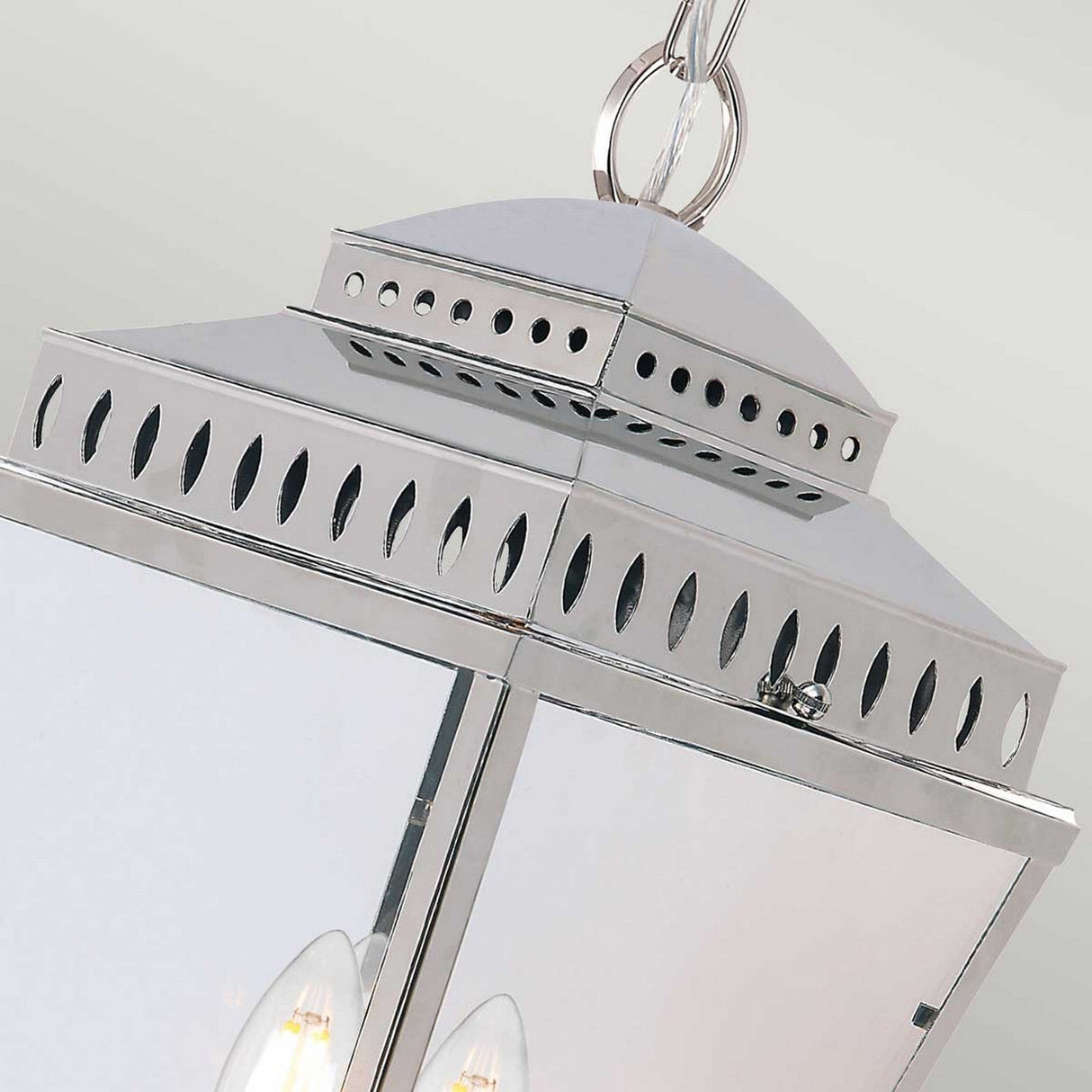 A detailed view of the Mansion 3 Light Outdoor Chain Pendant in polished nickel, featuring a modern geometric design. This pendant includes a suspension chain and boasts a reflective surface adorned with cut-out oval patterns near the top. The visible light bulbs inside enhance its sleek appeal.