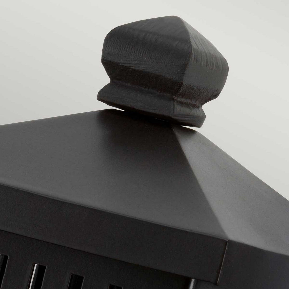 Close-up of the Matlock 1 Light Outdoor Wall Light in Old Bronze, showcasing rustic elegance with its geometric design. The cap features a pyramid shape topped by a small knob, all set against a light gray background.