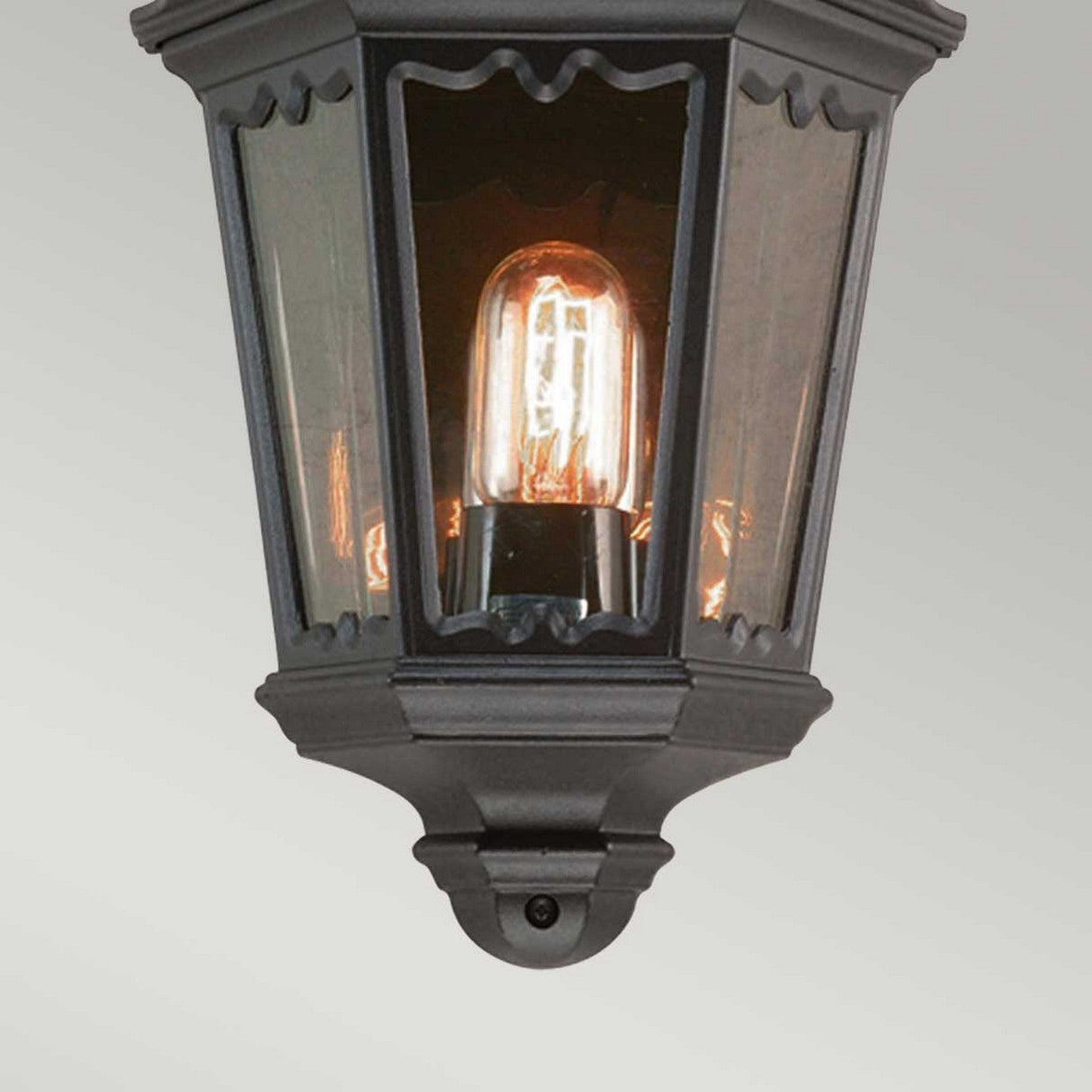 The Medstead 1 Light Outdoor Wall Light With PIR in black exudes vintage charm with its classic lantern design, clear glass enclosure, and exposed Edison bulb that casts a warm glow. Ideal for installation on a light-colored wall, it brings timeless elegance to any outdoor space.