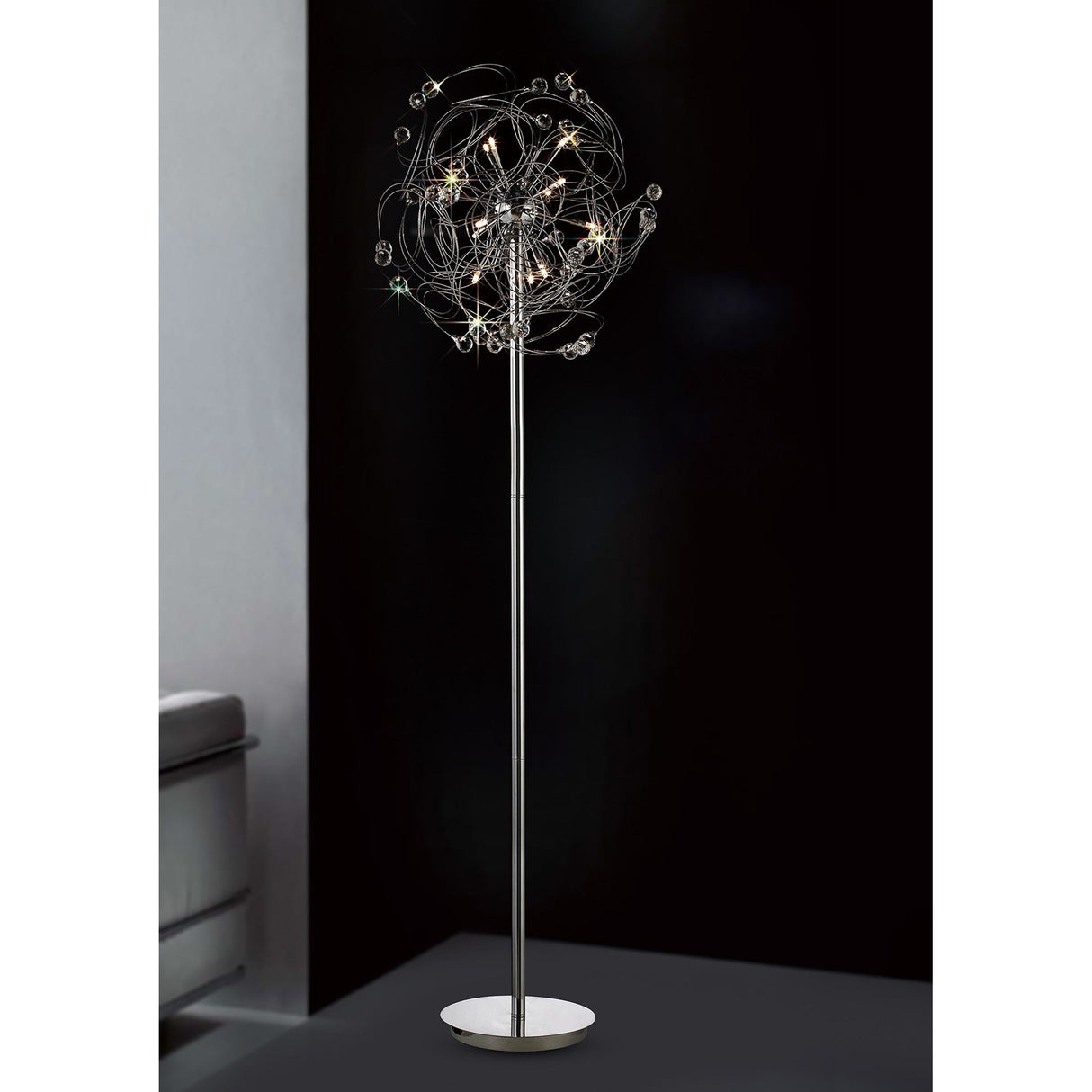 The Messe 12 Light Crystal Floor Lamp in polished chrome features a slim metallic stand and a decorative, starburst-inspired cluster of lights, creating striking ambient lighting against a dark backdrop.