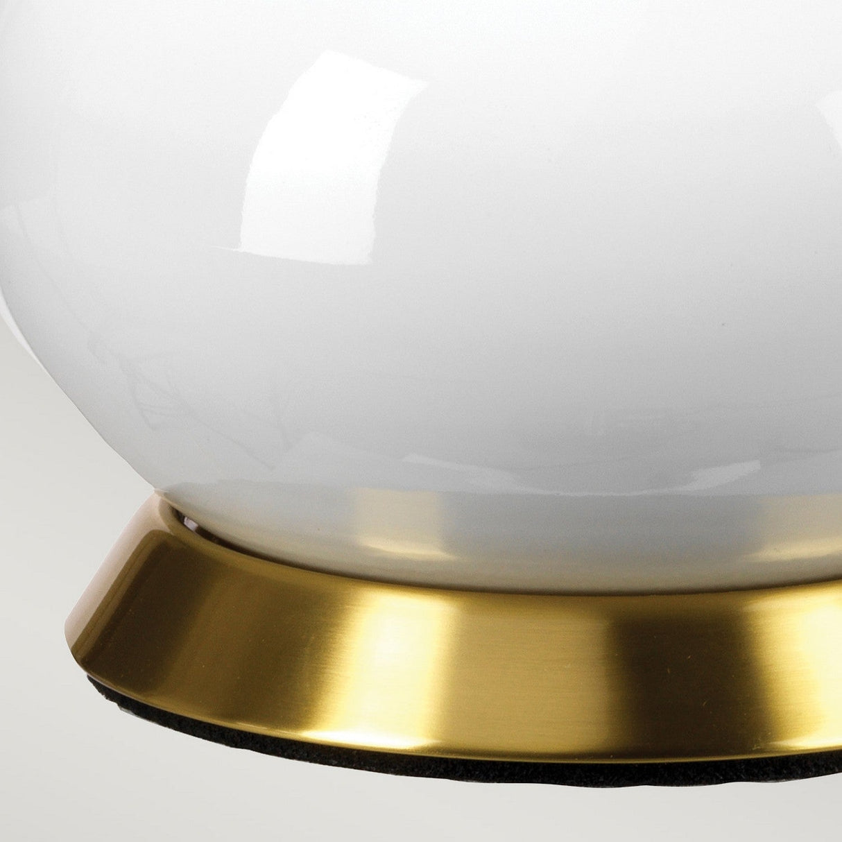 Close-up of the Milo 1 Light Table Lamp, featuring a shiny white ceramic base with an aged brass rim, set against a neutral background. The surface appears smooth and glossy.