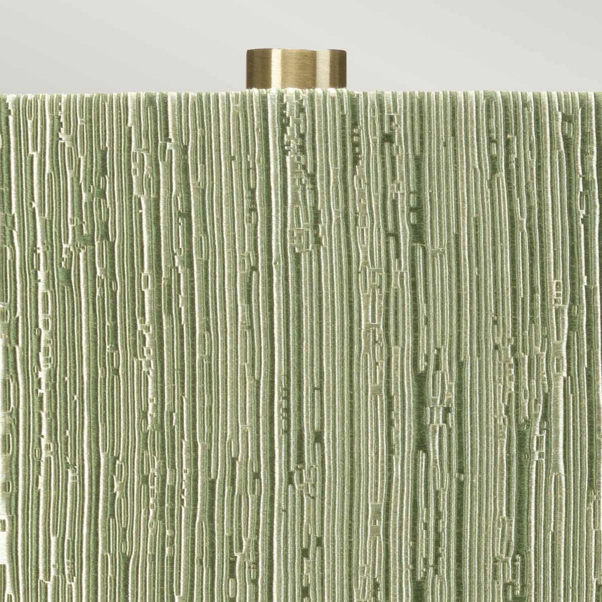 Close-up of the Milo 1 Light Table Lamp in aged brass and green, showcasing a decorative object with a textured surface that resembles vertical lines and grooves in shades of green. The aged brass, metallic cylindrical piece at the top suggests it's part of this elegant table lamp featuring a ceramic base.