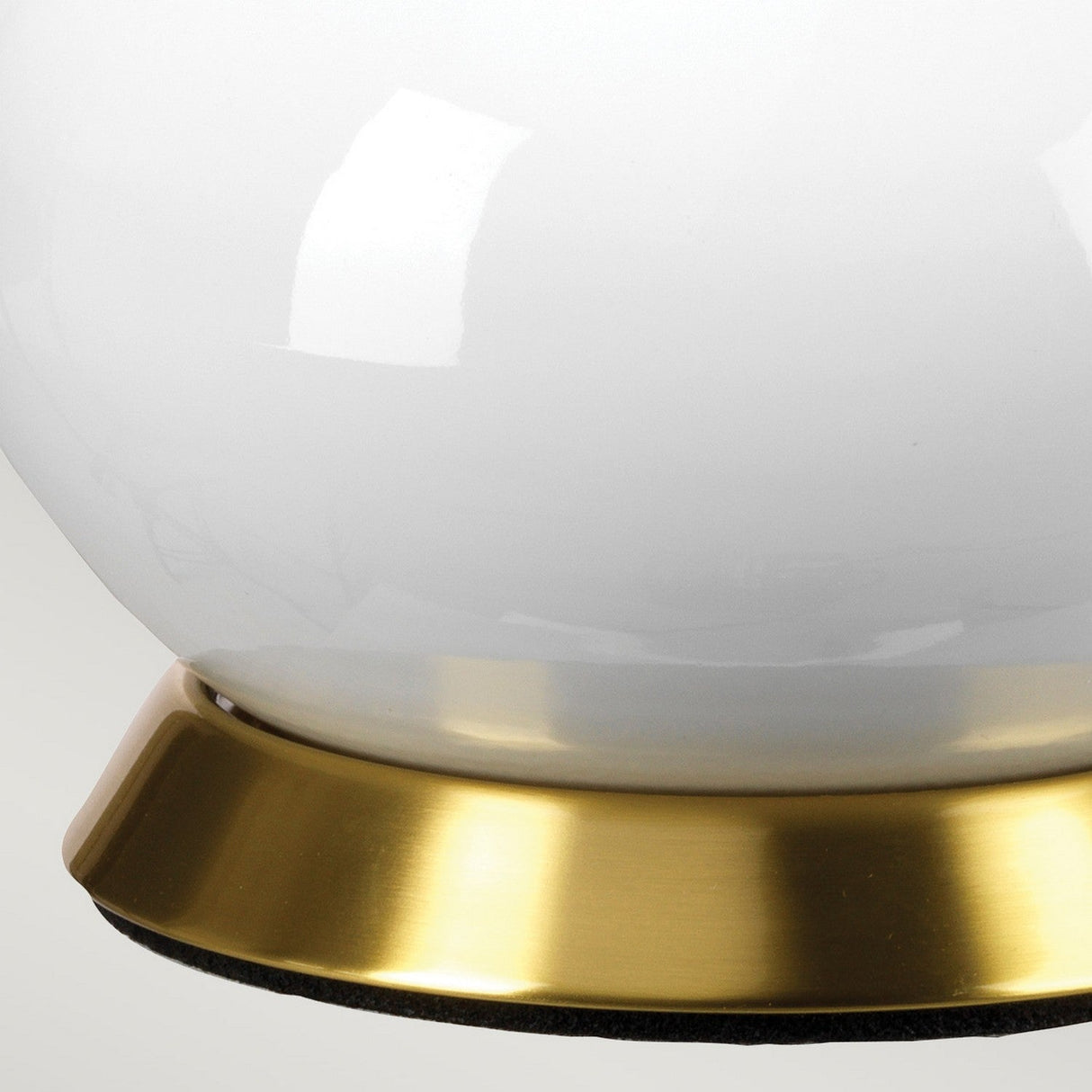 A close-up of the Milo 1 Light Table Lamp in Aged Brass/Green reveals its globe-shaped design with a refined aged brass base. The white surface of the lamp softly reflects light, creating a striking contrast with the polished metal beneath.
