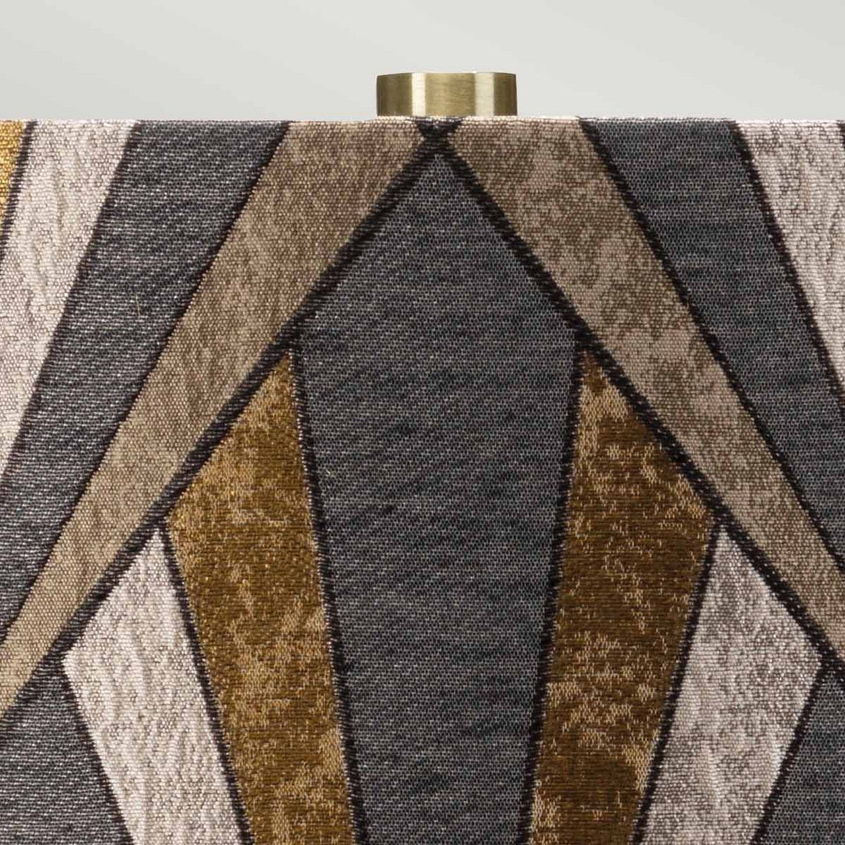 Close-up of the lampshade on the Milo 1 Light Table Lamp - Aged Brass/Brass, featuring a geometric pattern with triangular shapes in various shades of brown and gray. The top has an aged brass fitting that perfectly complements its elegant ceramic base.