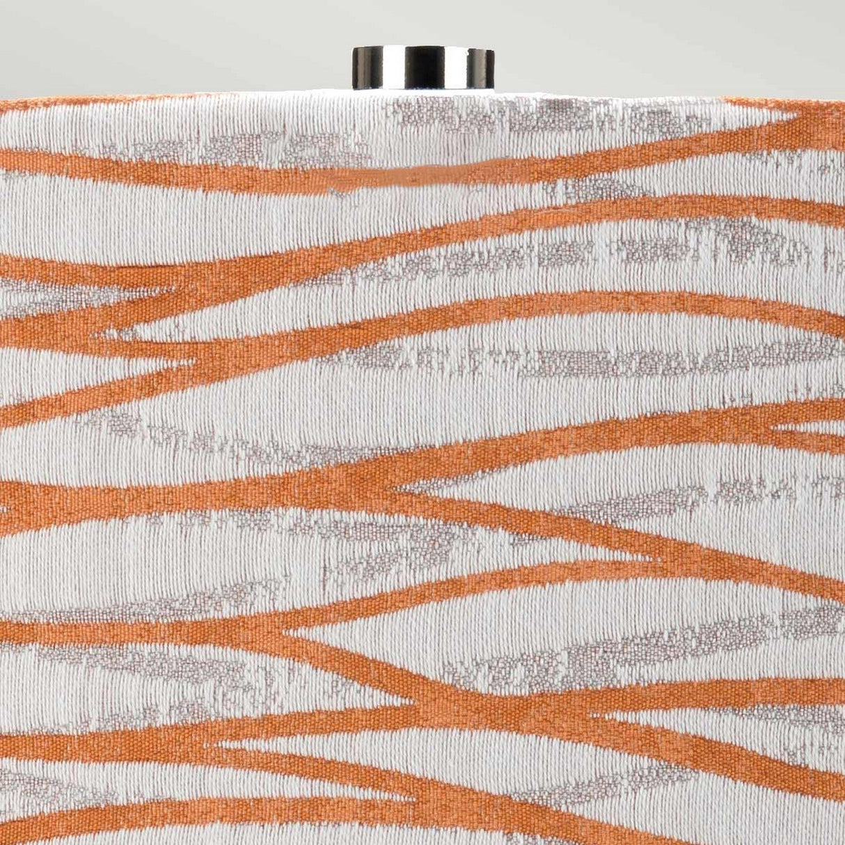Close-up of the Milo 1 Light Table Lamp showing an abstract fabric design with an orange shade and silver wavy lines on a white backdrop. The top edge features a metallic cylindrical cap with a polished nickel finish, partially visible.