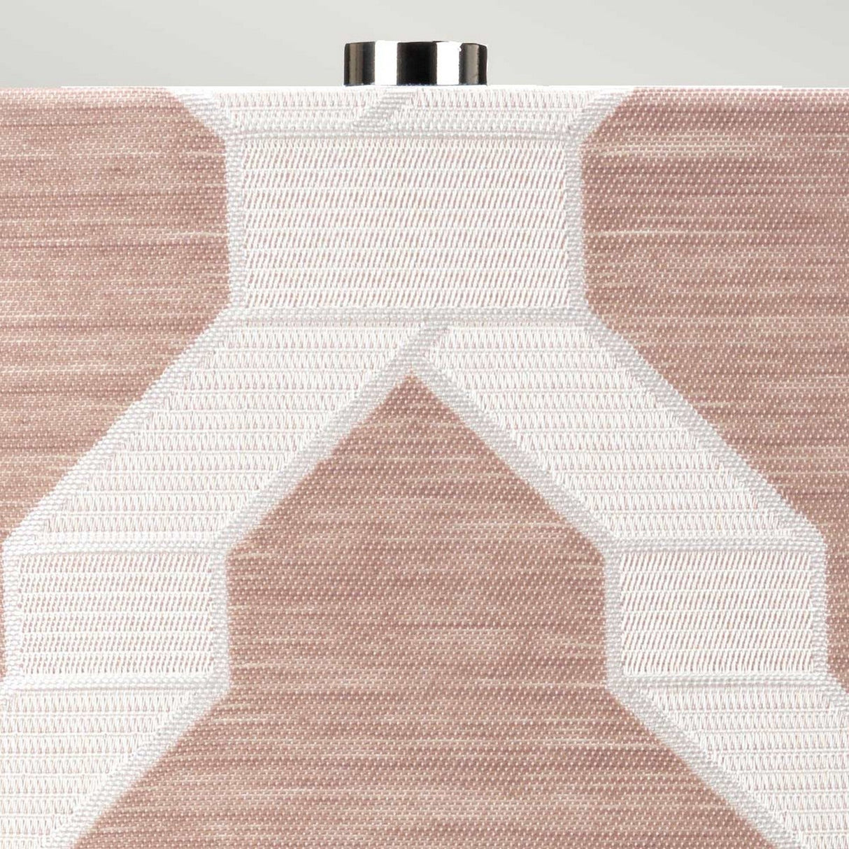 Close-up of a textured fabric showcasing geometric patterns in beige and white, complemented by the Milo 1 Light Table Lamp in polished nickel and pink, featuring a metallic fastening detail at the top edge.