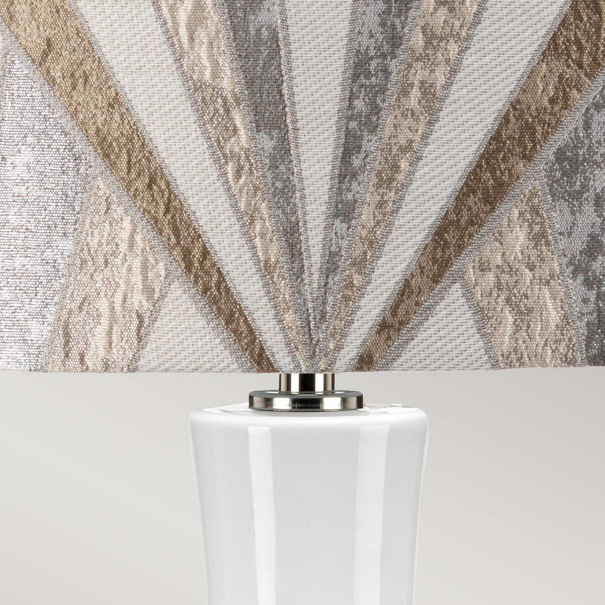 A close-up of the Milo 1 Light Table Lamp, featuring a geometric-patterned shade in brown and gray hues. The sleek ceramic base is white with a polished nickel accent connecting it to the shade.