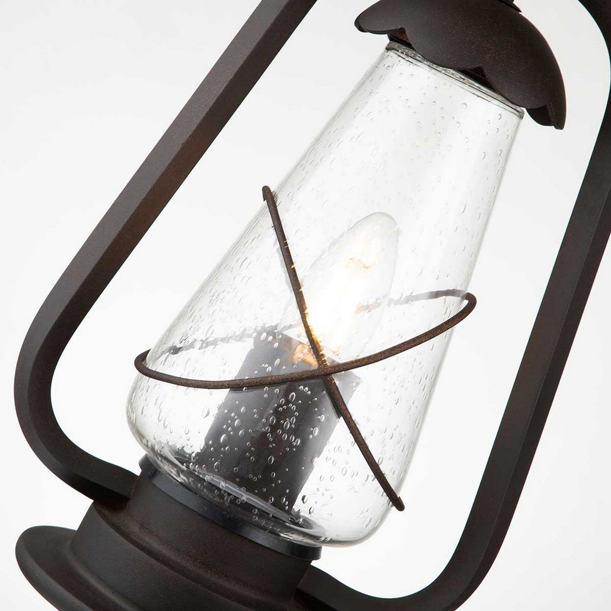 A close-up of the Miners 1 Light Outdoor Chain Pendant showcases its vintage lantern design featuring a glass casing with a lit bulb inside. This pendant, with its rustic metal frame in Old Bronze, exudes a warm, classic charm.