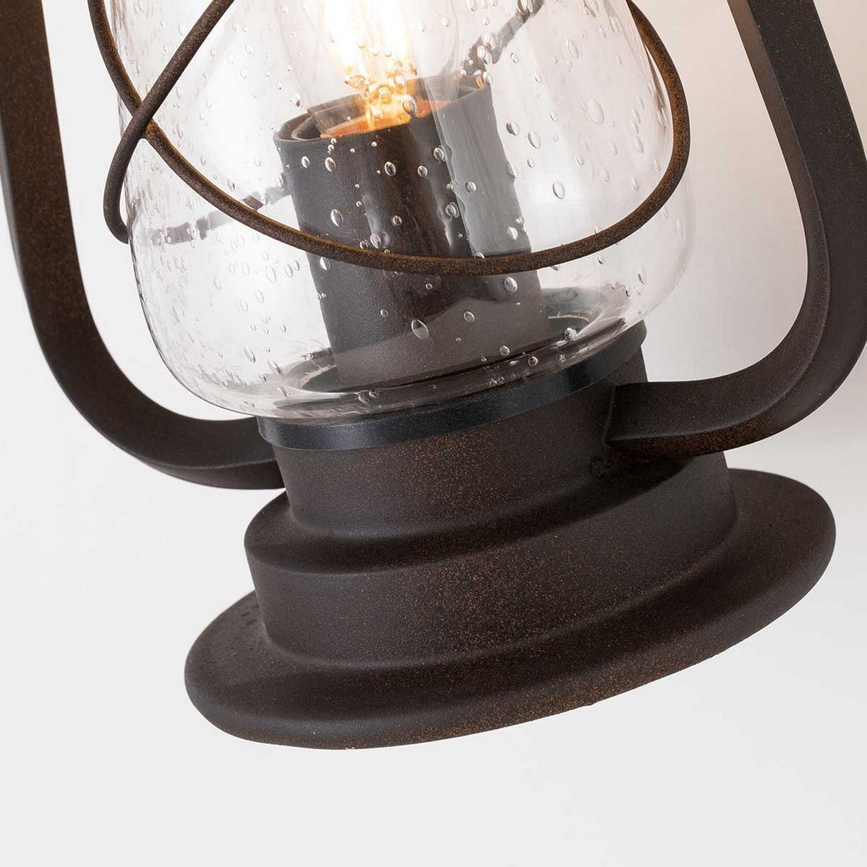 Close-up of the Miners 1 Light Outdoor Wall Light in Old Bronze, highlighting its vintage-style design with seeded glass and a glowing bulb inside. The lantern features a dark metal frame with a slightly weathered touch.