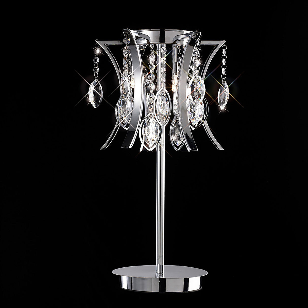 The Mios 3 Light Crystal Table Lamp in polished chrome features curved metal arms and hanging crystal decorations. Set against a black background, the crystals reflect light for a sparkling, luxury tabletop effect.