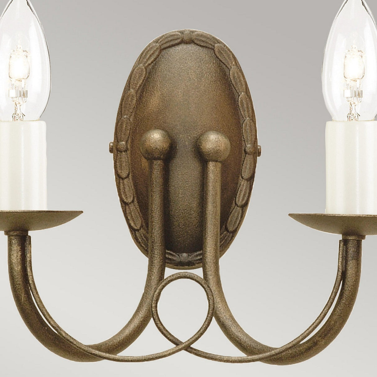 The Minster 2 Light Wall Light in Black/Gold Patina offers a vintage-style charm with its elegant design. It features two curved arms adorned with candle-shaped bulbs on round bases, beautifully mounted on an oval backplate with decorative edging to achieve a timeless look.