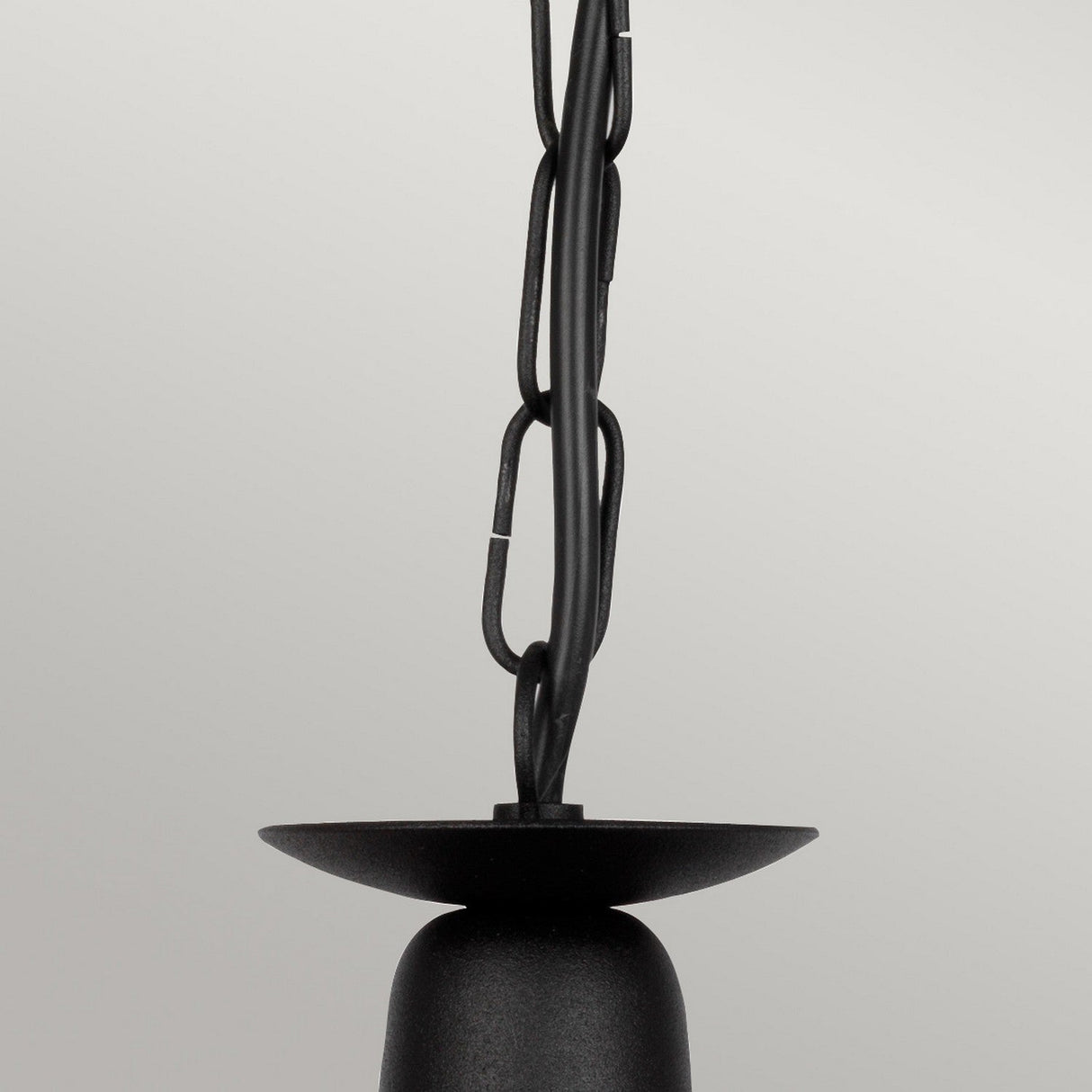 Close-up of the Minster 3 Light Chandelier in a sleek black finish, featuring a semi-flush fitting design with a curved base and a thick chain elegantly wrapped in wire. The background is a plain, light gray color.