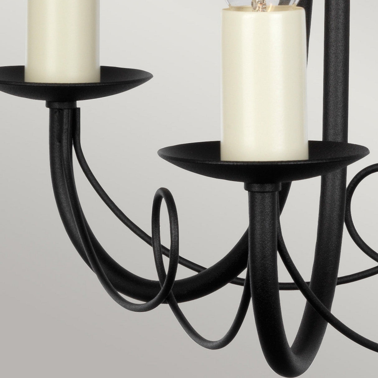 A close-up of the Minster 3 Light Chandelier in black features candle-shaped light bulbs and elegantly curved arms, highlighting its sleek, modern design. The sophisticated black finish stands out against a plain, neutral background.