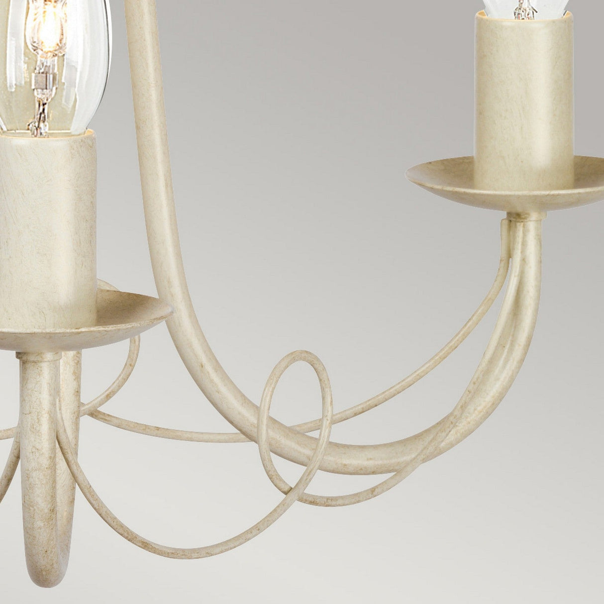 A close-up view of the Minster 3 Light Chandelier - Ivory/Gold Patina showcases two cream-colored candle-style bulb holders with elegantly curved gold patina metal arms, set against a simple gray background.