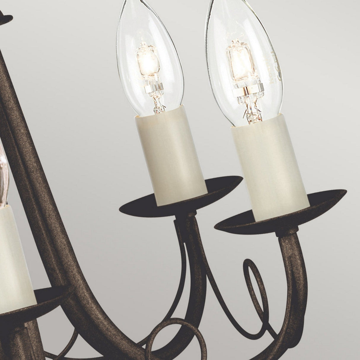 A close-up of the Minster 5 Light Chandelier - Black/Gold Patina showcases its convertible semi-flush fitting design, featuring two clear bulbs on intricately curved metal arms. The chandelier's black with gold patina finish adds a touch of vintage elegance against the neutral background.