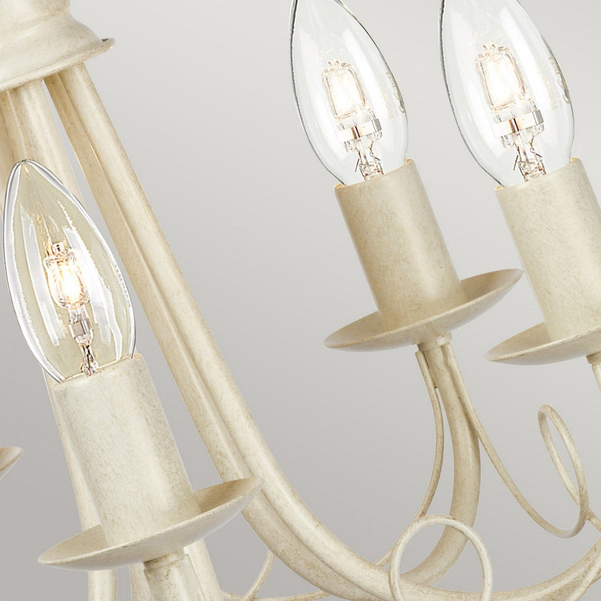 Close-up of the Minster 5 Light Chandelier - Ivory/ Gold Patina, showcasing candle-shaped light bulbs and elegant, curved metalwork in a cream-colored finish against a plain background.