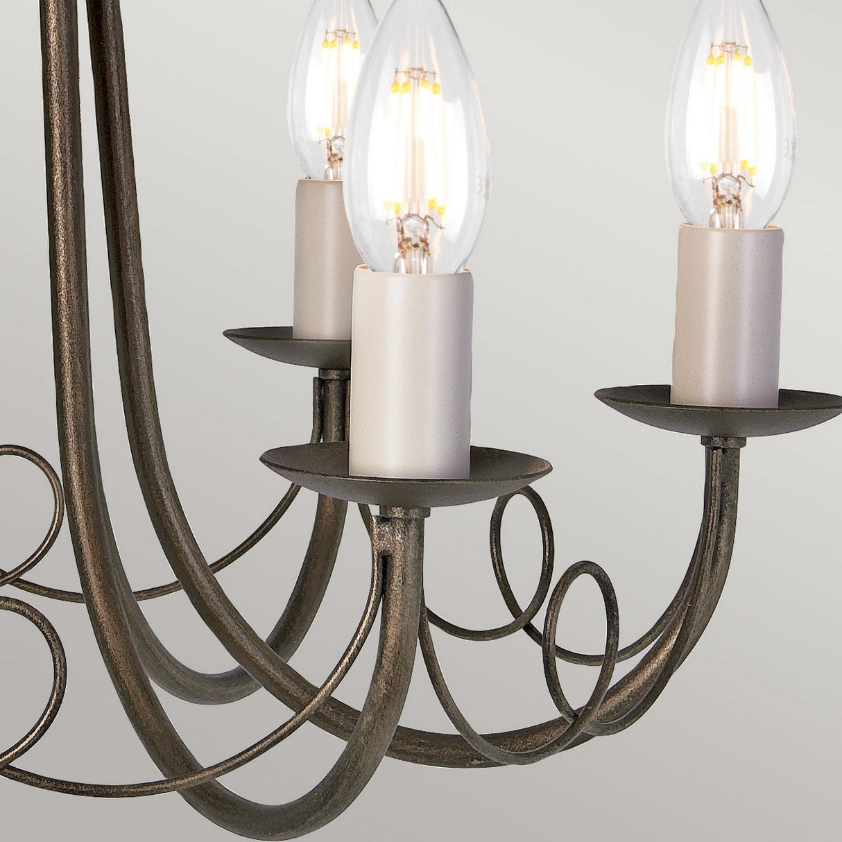 Close-up of the Minster 6 Light Chandelier, showcasing its vintage-style black frame with a gold patina. It features three candle-shaped LED bulbs, elegantly curved metalwork, and a classic bronze finish for an exquisite look.