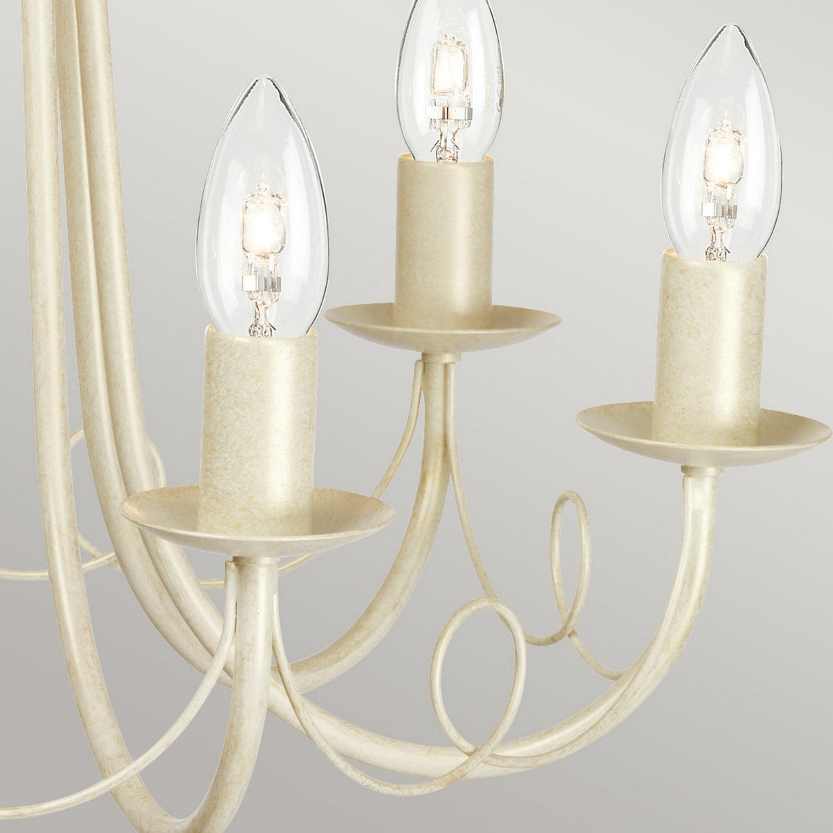 Close-up of the Minster 6 Light Chandelier in ivory and gold patina, showcasing its elegant design with three candle-shaped light bulbs. The fixture features gracefully curved arms and exudes a classic, minimalist charm against a neutral background.