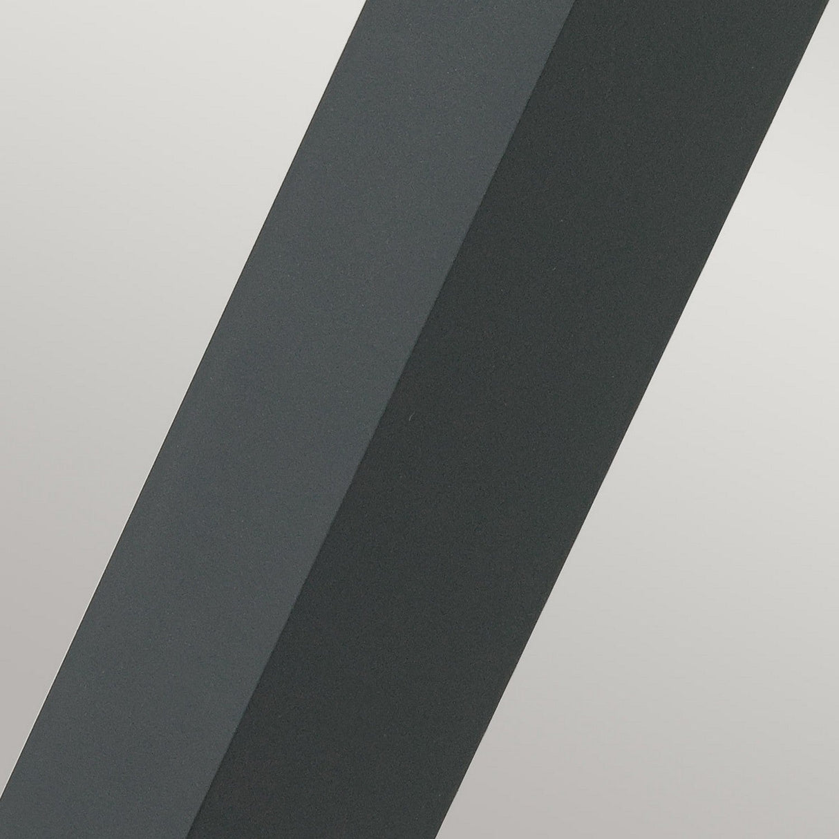 A close-up of the Molde LED Bollard - Graphite showcases a geometric composition with two intersecting shapes, one in deep graphite gray and the other in a lighter shade. The design, reminiscent of die-cast aluminum artistry, forms an abstract pattern featuring contrasting colors and sharp, clean lines.