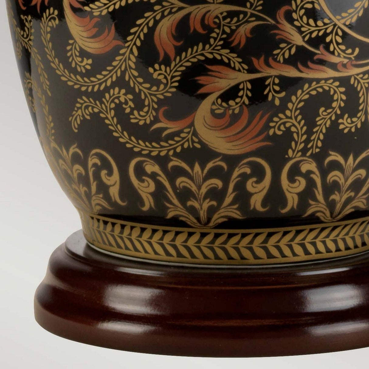 Close-up of the Morris 1 Light Small Table Lamp, featuring an ornate ceramic design with intricate floral and leaf patterns in gold and black hues, evocative of a Chinese porcelain lamp. The lamp sits on a polished wooden base, showcasing its decorative craftsmanship.