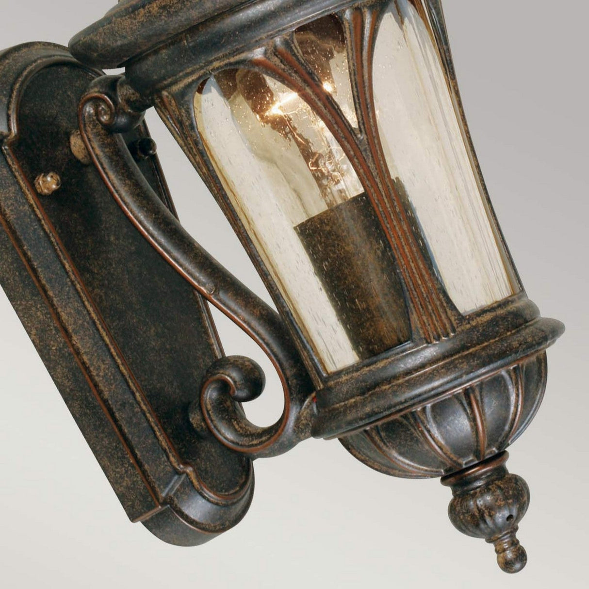 Introducing the New England 1 Light Outdoor Wall Light in Weathered Bronze, a vintage-style lantern with hand-blown glass panels and an exposed bulb. This piece showcases ornate metalwork, offering a rustic, antique appearance for your outdoor spaces.