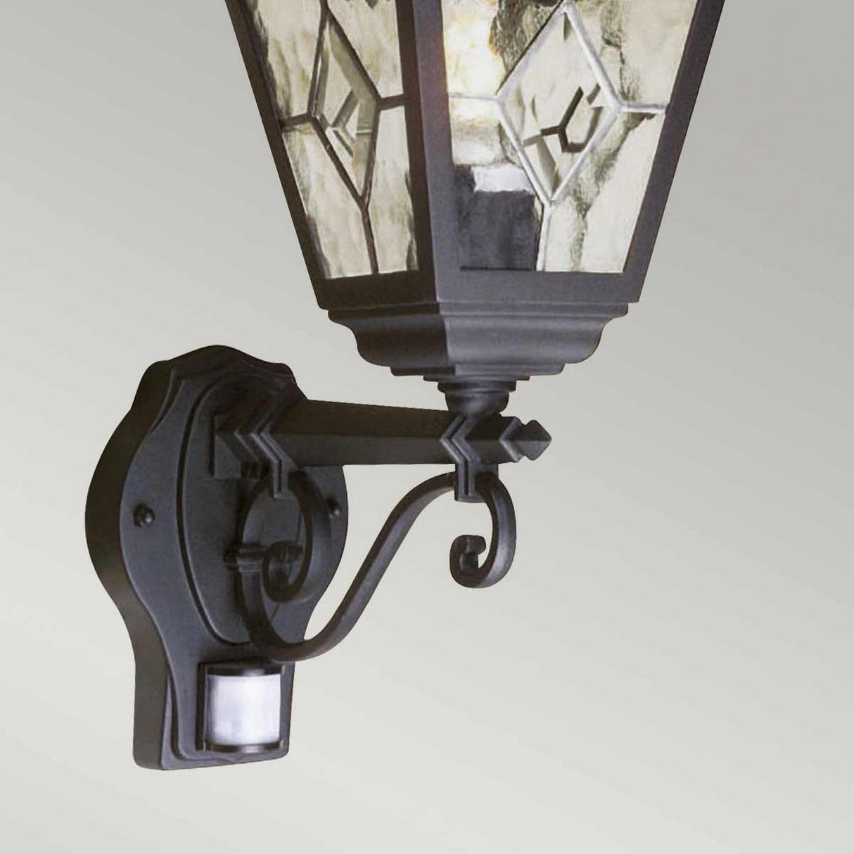 Close-up of the Norfolk 1 Light Up Outdoor Wall Light with PIR - Black, highlighting its decorative stained glass panels and detailed black metal frame. Built for outdoor durability, this lantern features a discreetly positioned PIR motion sensor at its base.