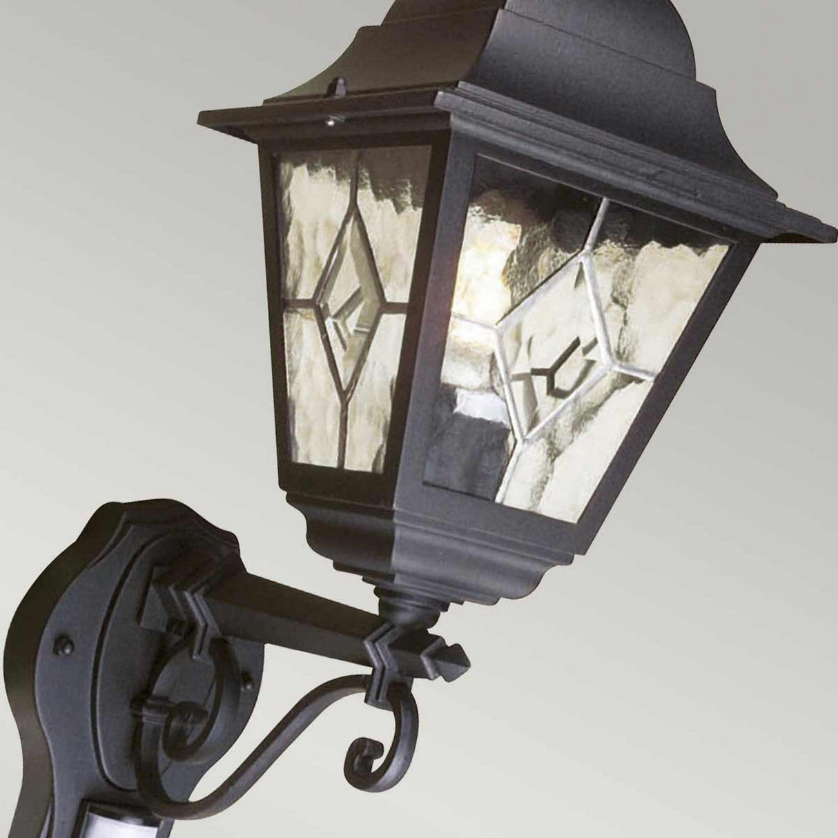 The Norfolk 1 Light Up Outdoor Wall Light with PIR - Black is a vintage-style lantern featuring decorative glass panels and a black metal frame accented by intricate scrollwork. Known for its outdoor durability, this elegant fixture enhances any space with charm and functionality.