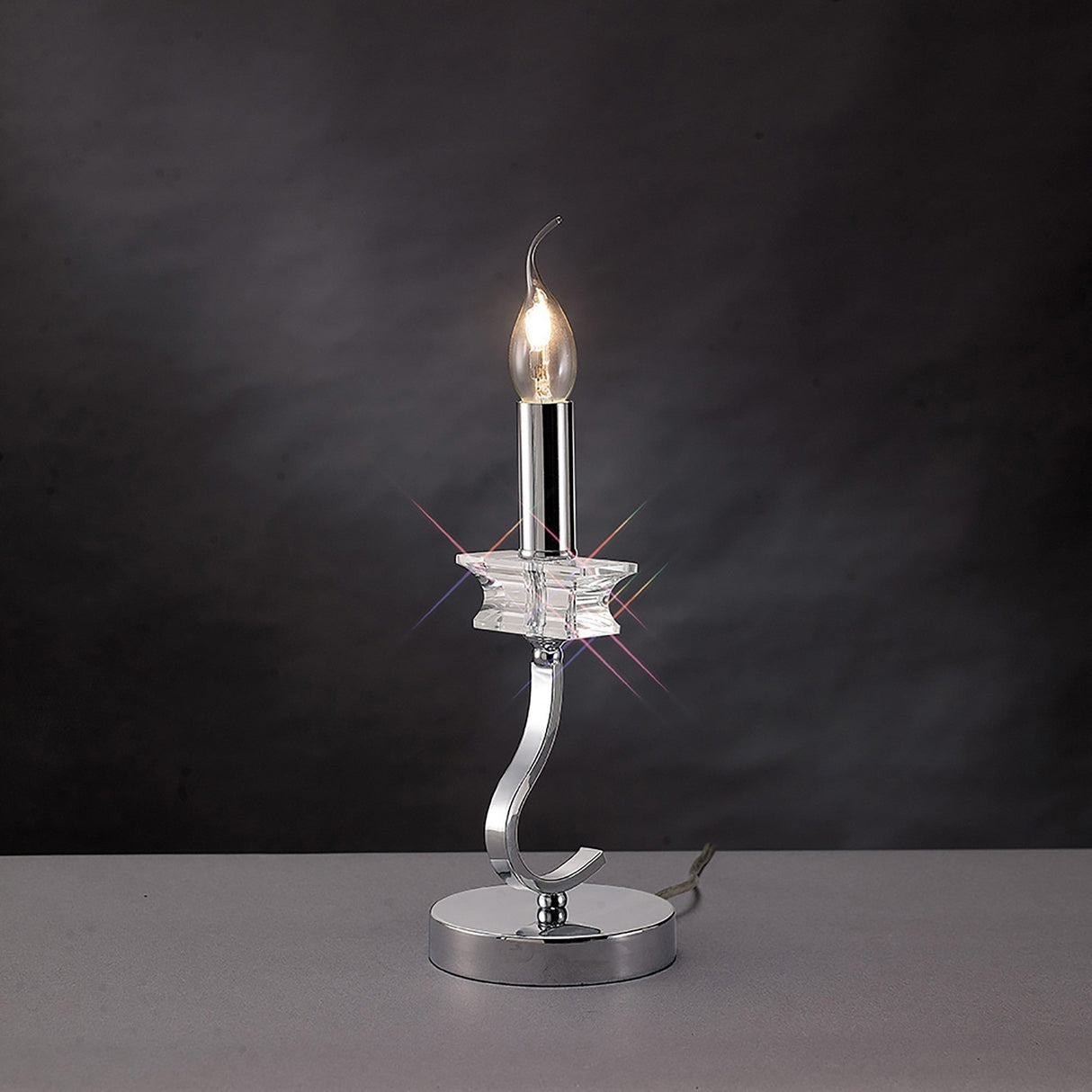 The Nydia 1 Light Crystal Table Lamp features a polished chrome base, curved stem, star-shaped crystal accent, and dimmable lighting that glows beautifully against a dark background.