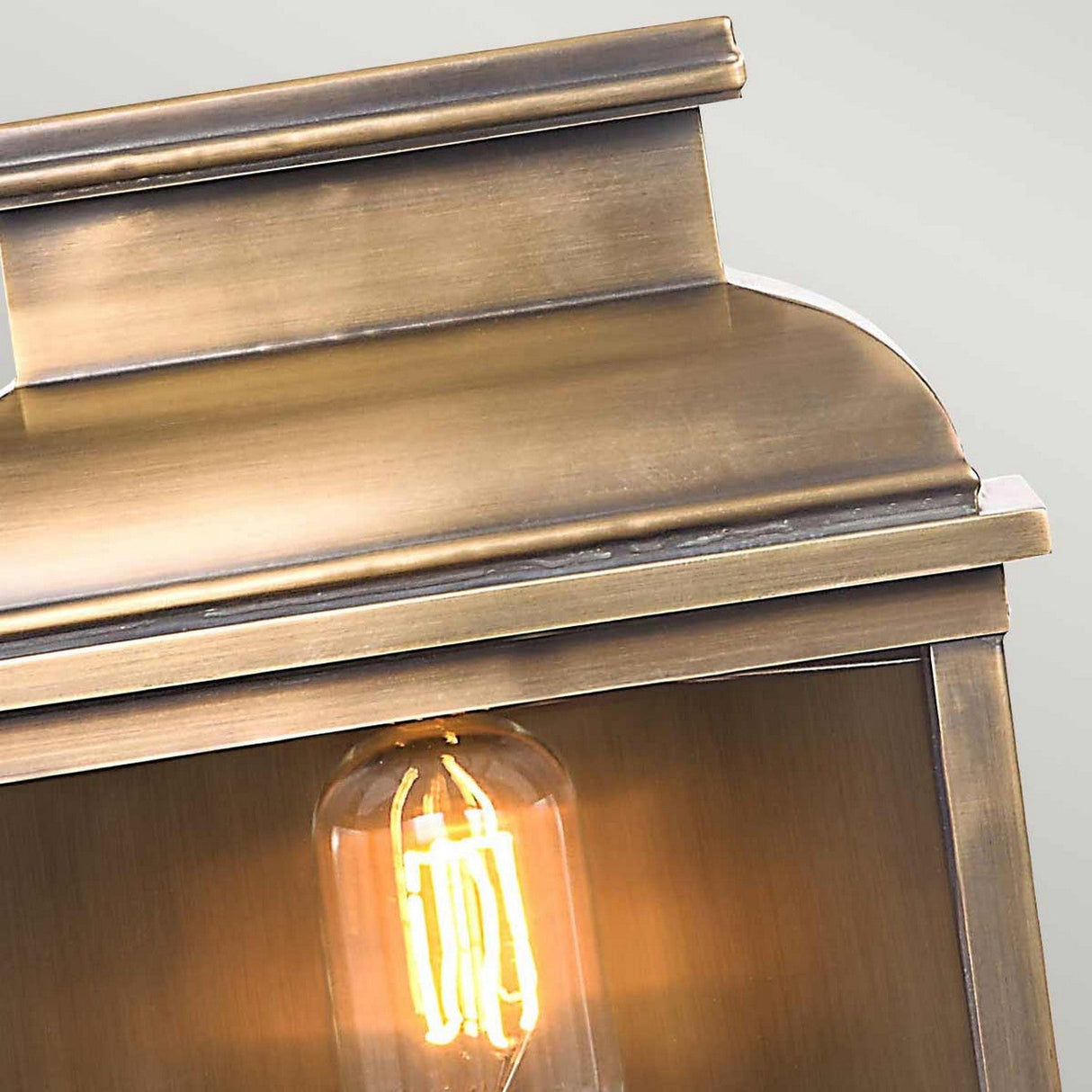 A close-up of the Old Bailey 1 Light Outdoor Wall Light in aged brass showcases a vintage-style lantern with a glowing exposed filament bulb. The lantern, made from solid brass, flaunts a smooth metallic finish and an antique design, offering an elegant and classic appearance ideal for outdoor use.