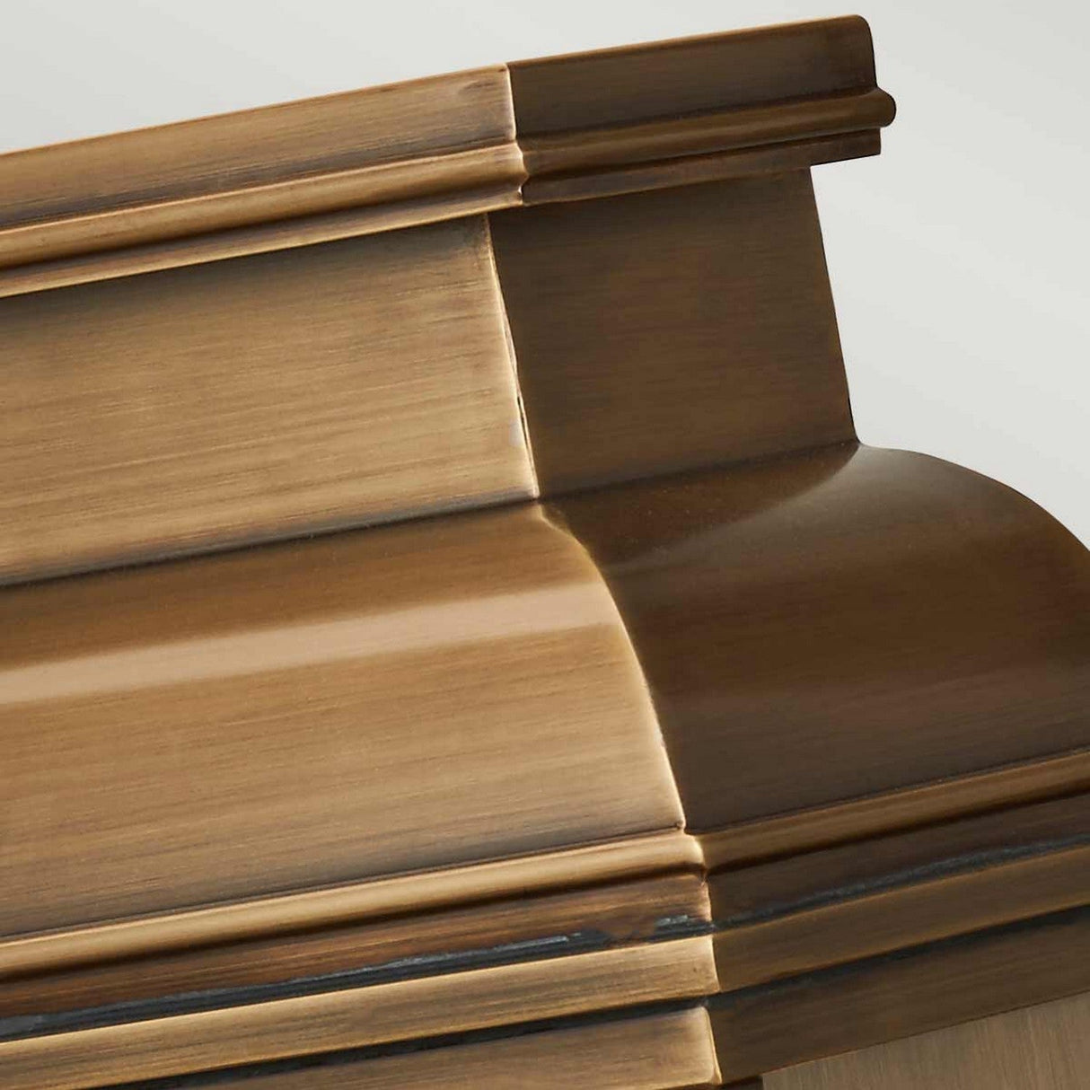 Close-up of a polished wooden coffin with intricately carved details and a smooth finish, resembling the elegance of the Old Bailey 2 Light Outdoor Wall Light in aged brass craftsmanship. The image focuses on a corner section, displaying the grain and rich brown color of the wood akin to such an elegant finish.