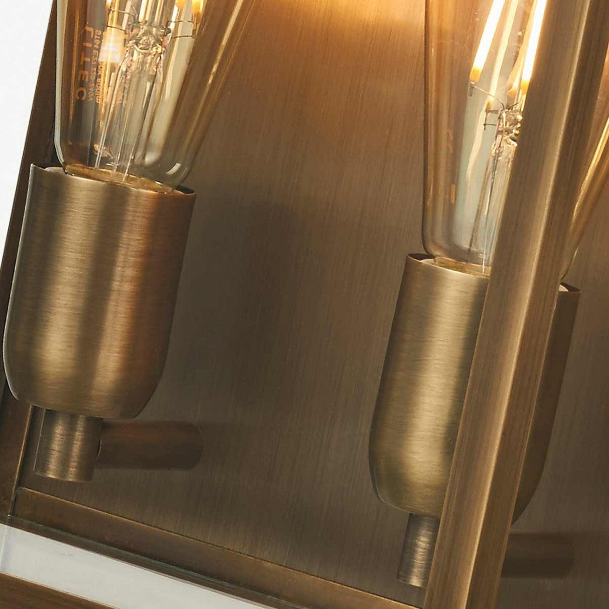Close-up of the Old Bailey 2 Light Outdoor Wall Light in aged brass, featuring vintage-style Edison bulbs that emit a warm glow. The fixture's polished metallic surface enhances the reflective effect, highlighting its aged brass finish.