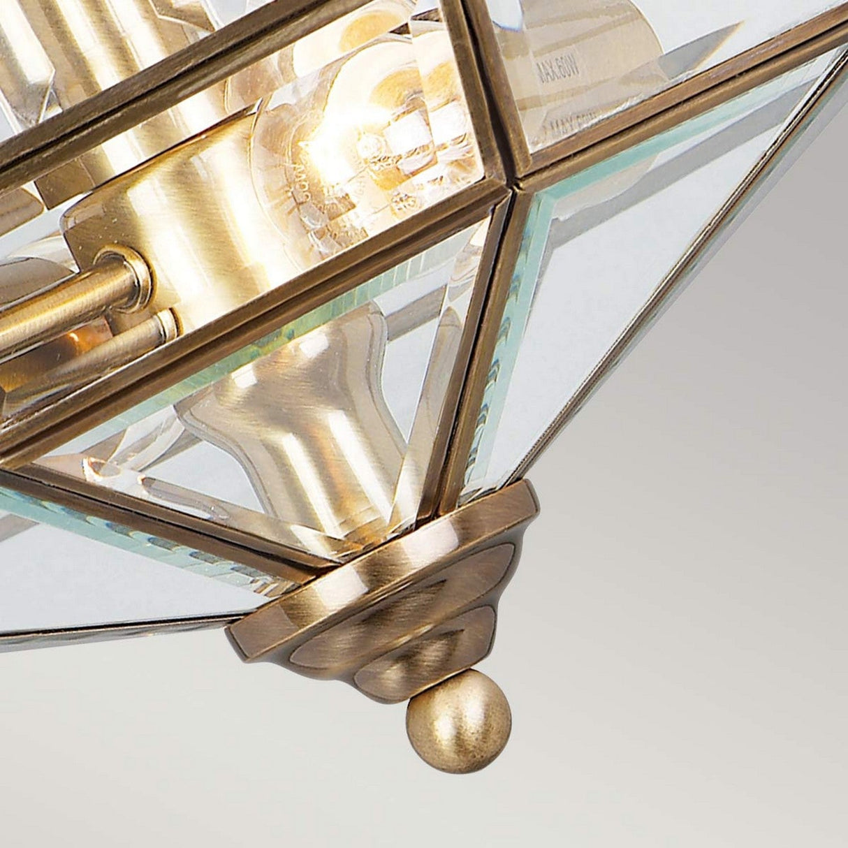 Close-up of the Old Park 2 Light Semi Flush in Antique Brass, highlighting its design with triangular glass panels and solid brass construction, finished with a decorative brass finial at the bottom.
