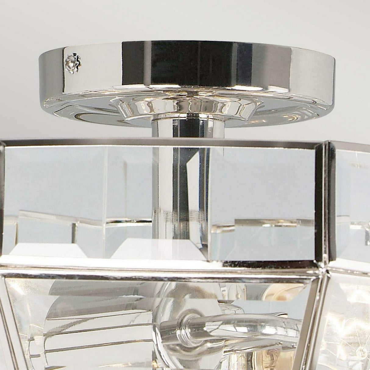 Close-up of the Old Park 2 Light Semi Flush in polished nickel, featuring a geometric design and clear panels. The fixture prominently showcases the light bulb through its panels, and the metal finish beautifully reflects its surroundings.