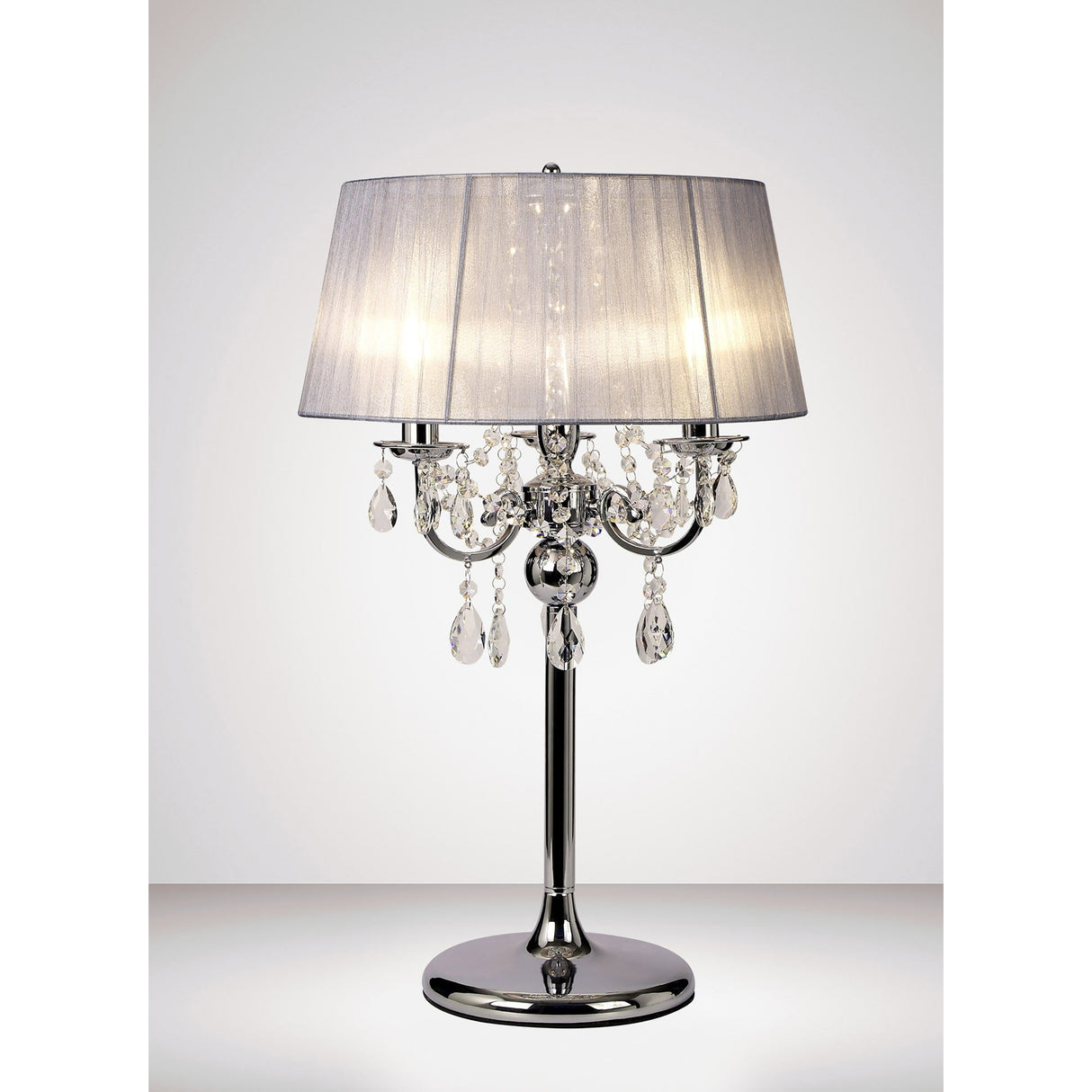 The Olivia 3 Light Crystal Table Lamp features a polished chrome base, grey shade, and hanging crystal accents, offering elegant ambient lighting against a plain white background.