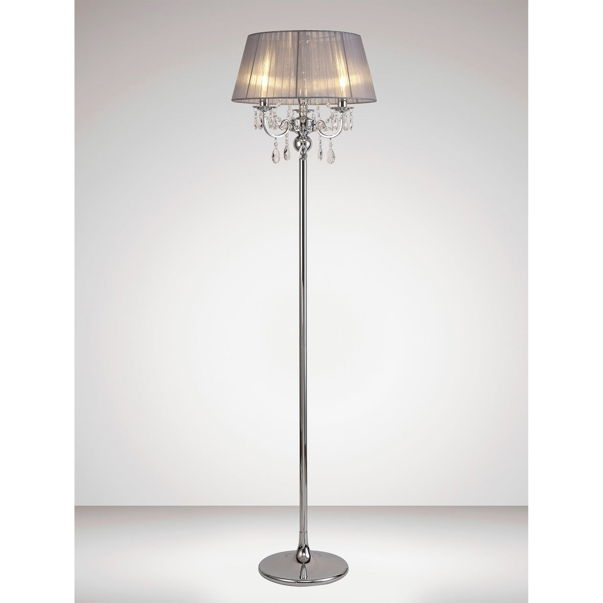 The Olivia 3 Light Crystal Floor Lamp features a chrome finish, grey shade, and hanging crystal accents, making it a modern addition to any softly lit room with a plain background.