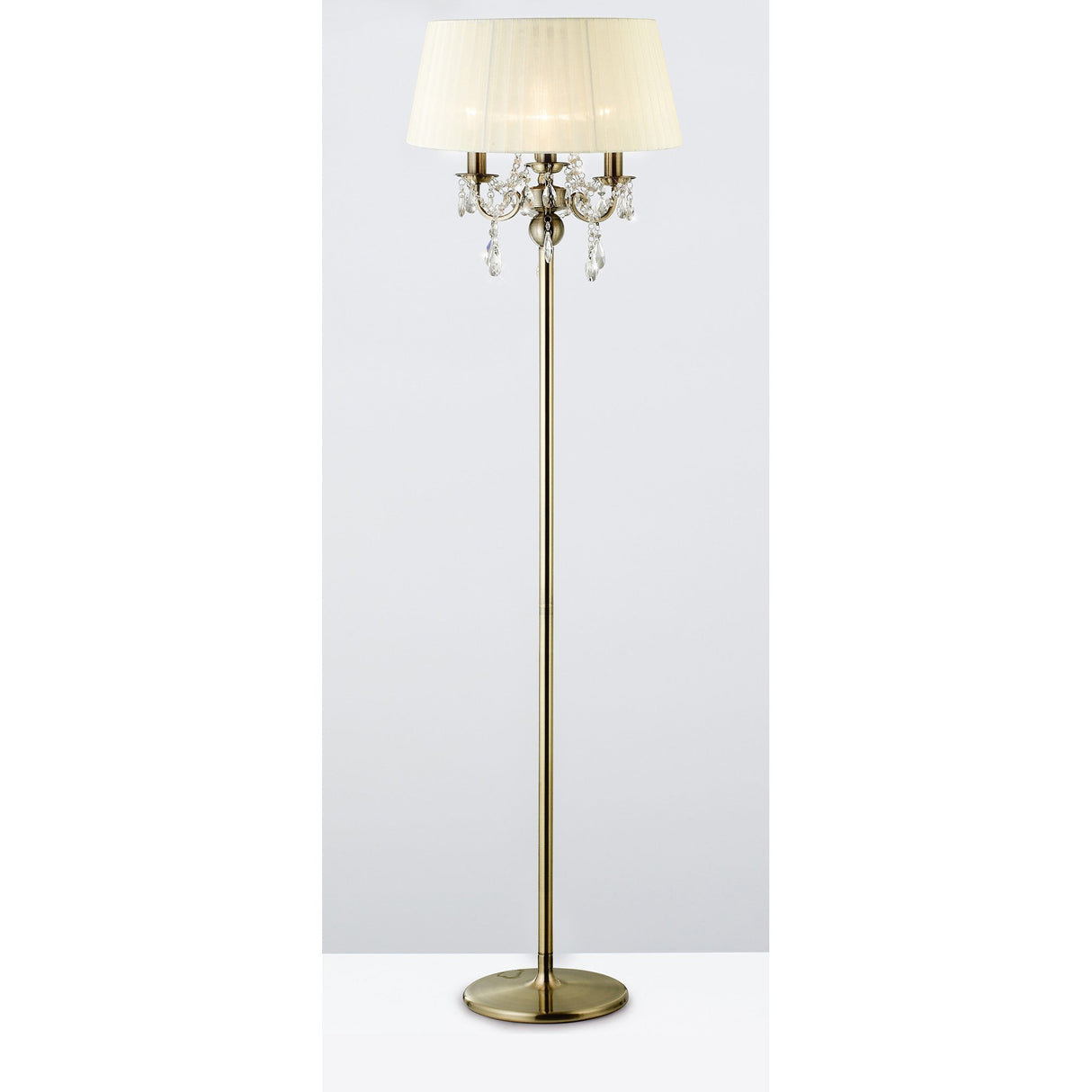 The Olivia 3 Light Crystal Floor Lamp features a tall antique brass frame, cream pleated shade, round base, and elegant hanging crystal accents, shown here against a simple light background.