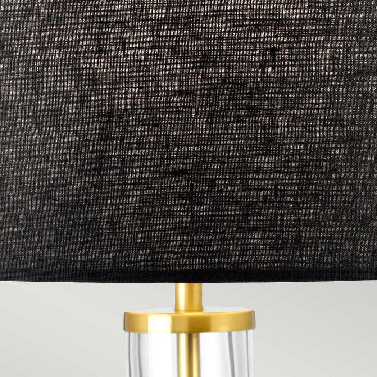 Close-up of the Orb 1 Light Table Lamp - Aged Brass With Black Shade, showcasing a textured black shade and a sleek, transparent base with an aged brass detail. The background is a neutral light gray.