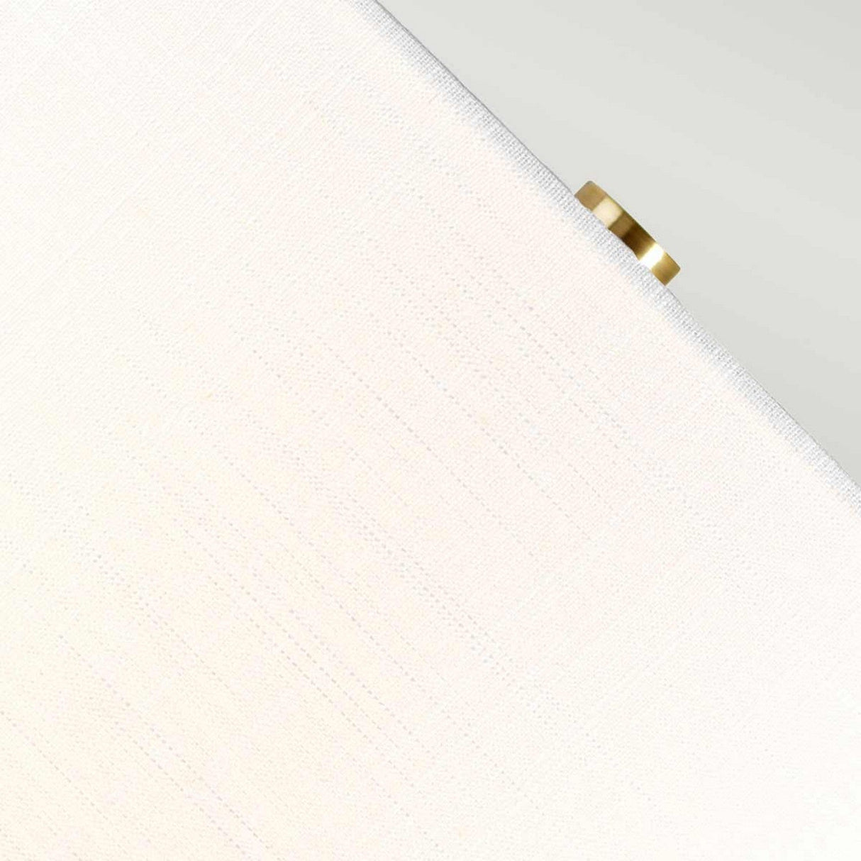 Close-up of a textured white surface resembling the White Shade of the Orb 1 Light Table Lamp, with a small, round detail in an Aged Brass finish positioned at the top right corner. The image is angled, producing diagonal lines across the frame.