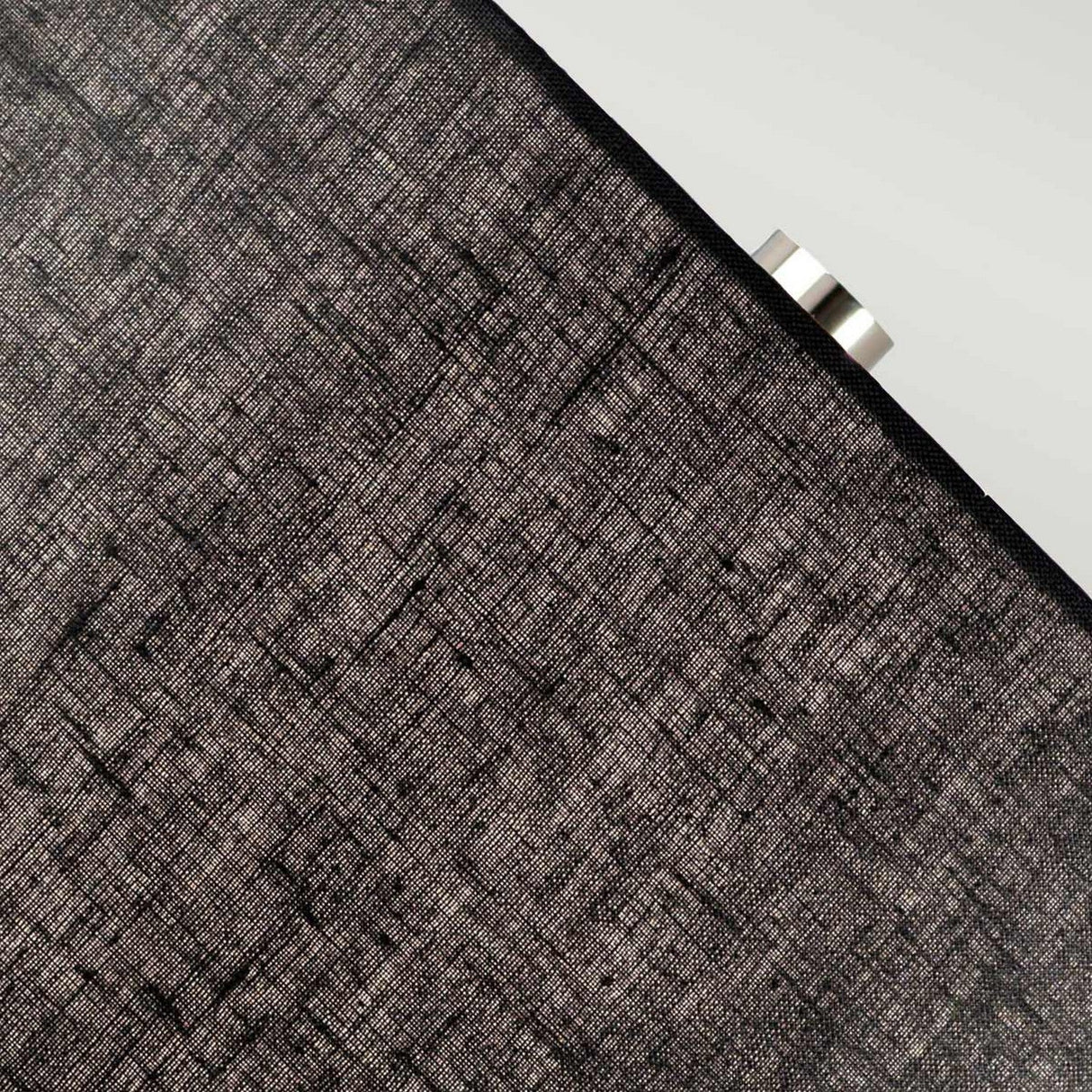 Close-up of the black shade from the Orb 1 Light Table Lamp, featuring a subtle crisscross pattern, partially obscuring a light source behind it, similar to its soft glow. The shade gleams with a polished nickel-like sheen, revealing a metallic element peeking out on the right side.