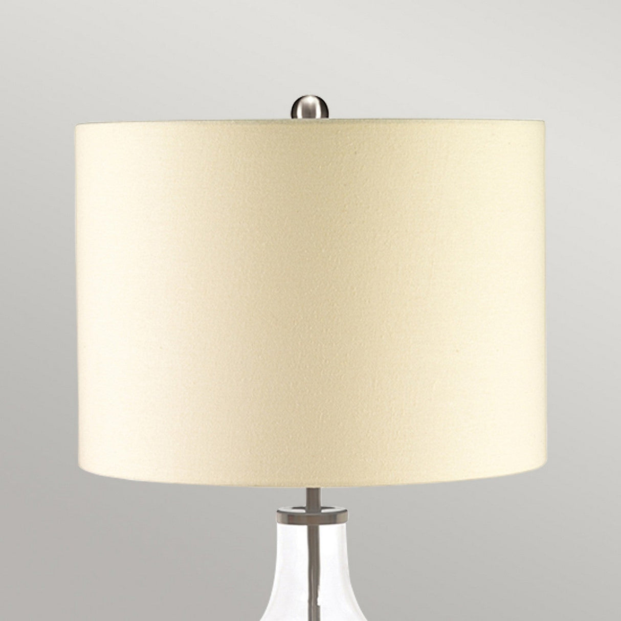 A close-up of the Orb 1 Light Table Lamp in clear glass with a beige shade, set against a neutral gray background.