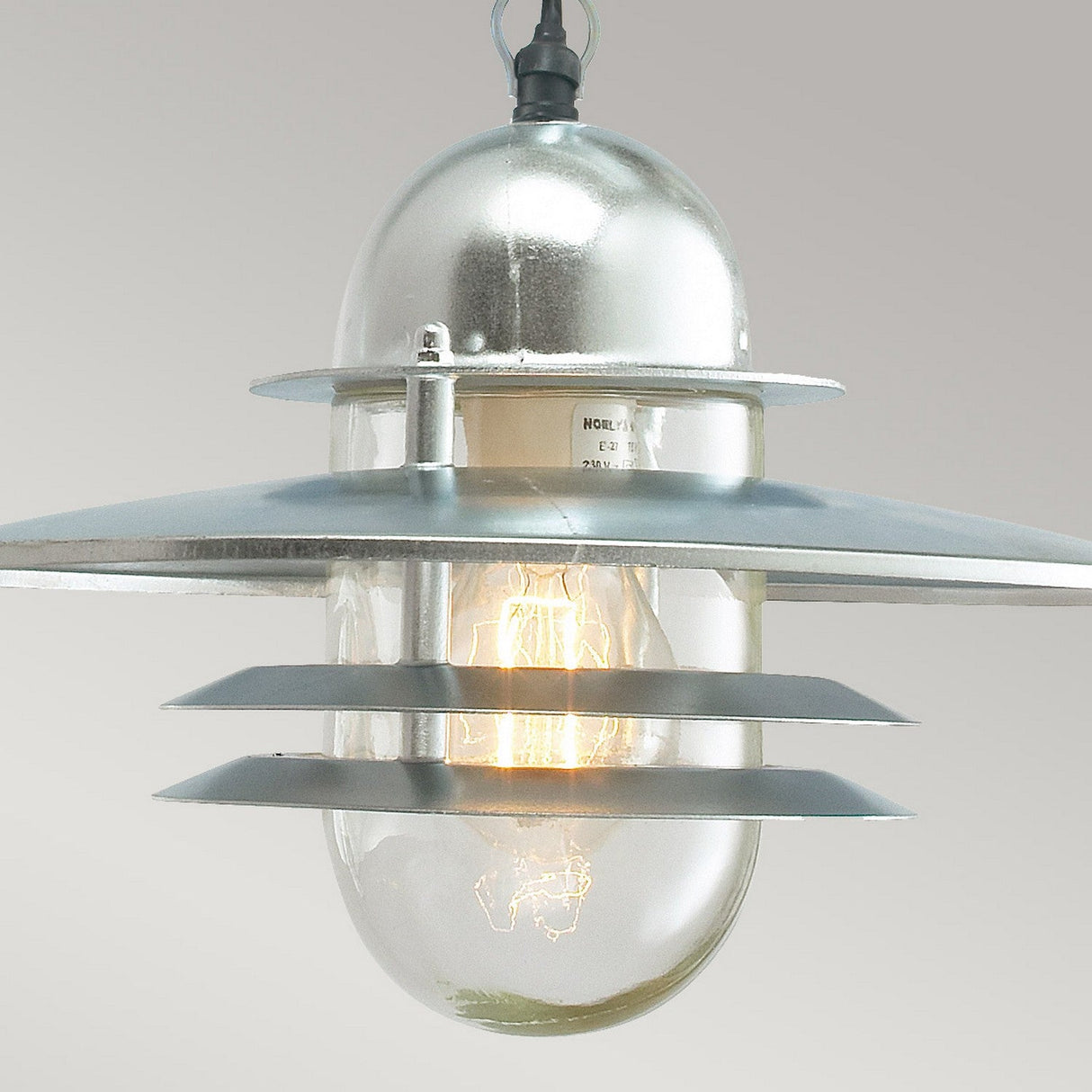 The Oslo Outdoor 1 Light Chain Pendant in Silver features a modern industrial style with galvanized steel finish and layered circular shades. Its transparent casing makes the light bulb visible, offering a sleek Scandinavian design perfect for any space.