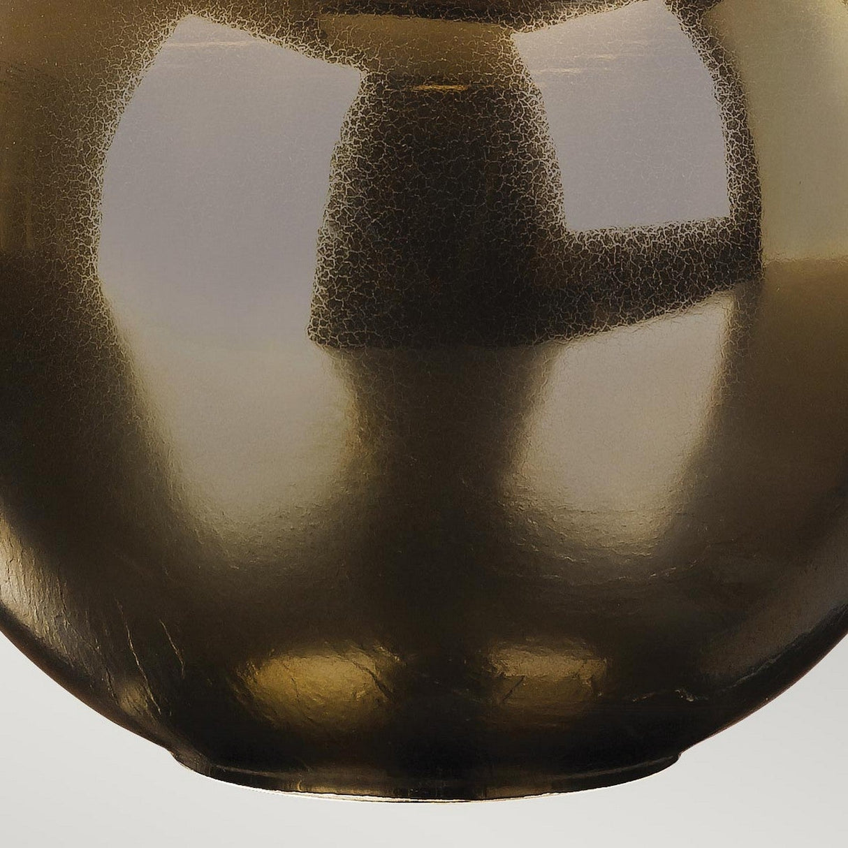 Close-up of a bronze metallic spherical object with a textured, crackled surface pattern, its mirrored reflections reminiscent of the Ottoman 1 Light Table Lamp with Ivory Shade, set against a light background.
