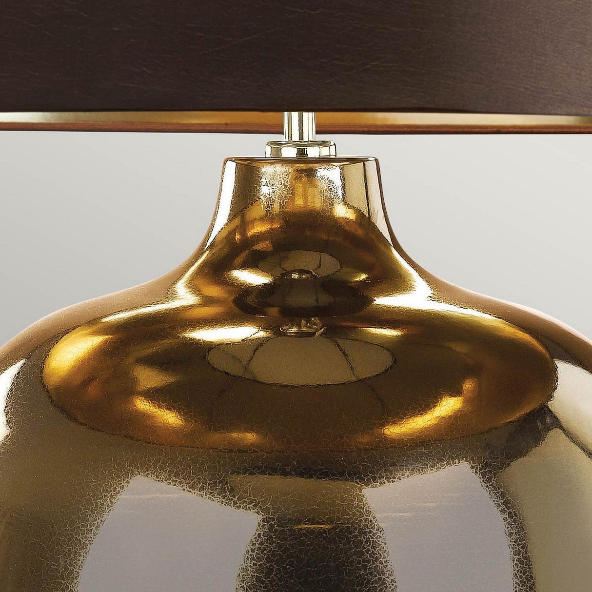 Here's a description using the given product data:
A close-up of the Ottoman 1 Light Table Lamp showcases its bronze metallic surface with a glossy reflective sheen. The lamp features an elegant curved design and is topped with a dark brown faux silk shade, lined with gold. The sleek exterior beautifully reflects the ceiling light.